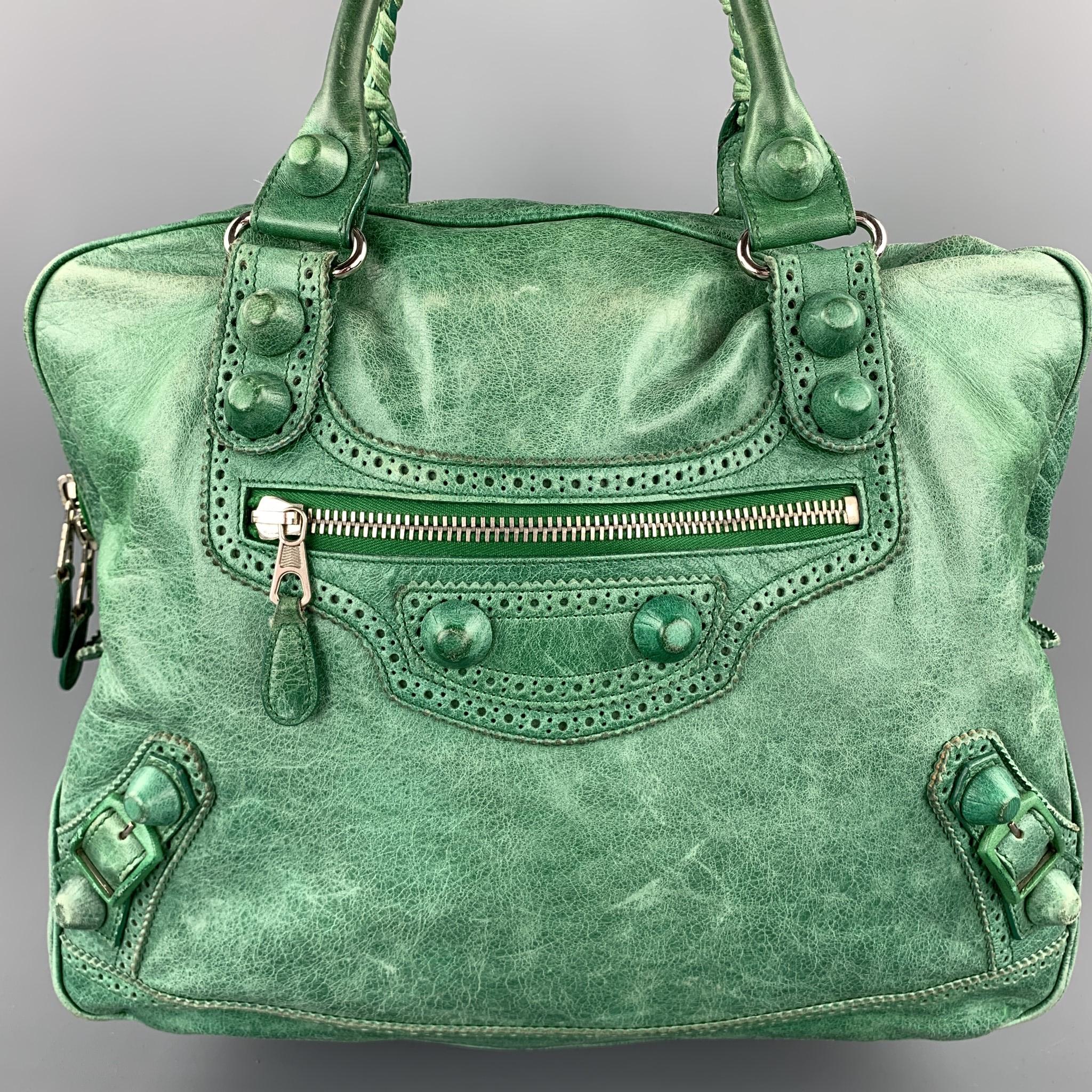 BALENCIAGA handbag comes in a green distressed leather with perforated details featuring braided top handles, large stud embellishments, silver tone hardware, inner zipper pocket, and a full zip closure. Made in Italy.

Good Pre-Owned
