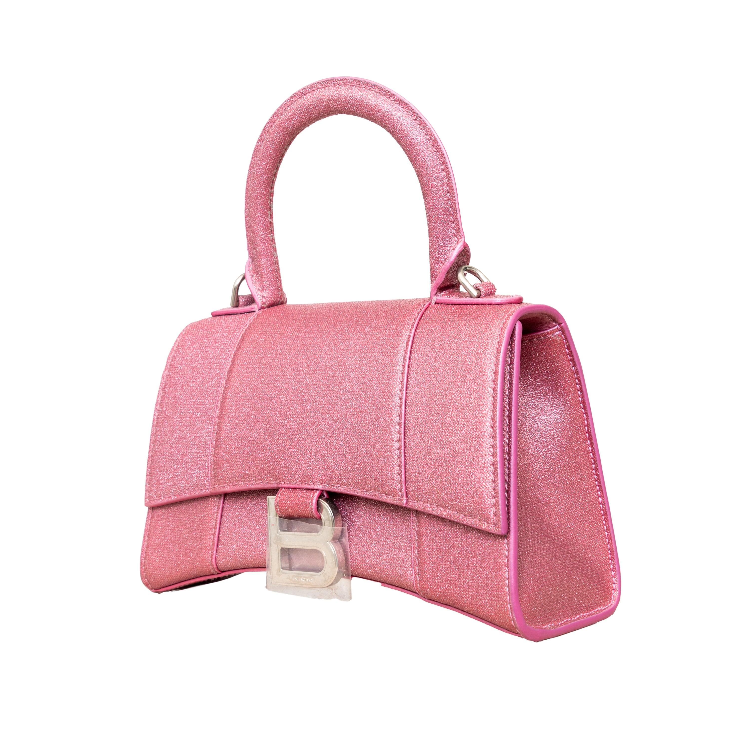 Crafted from pink, glitter embellished calfskin, this Balenciaga handbag in XS format features the iconic curvilinear base, one top handle, and a studded magnet closure for a chic and modern touch. The aged-silver B logo hardware and nappa lambskin