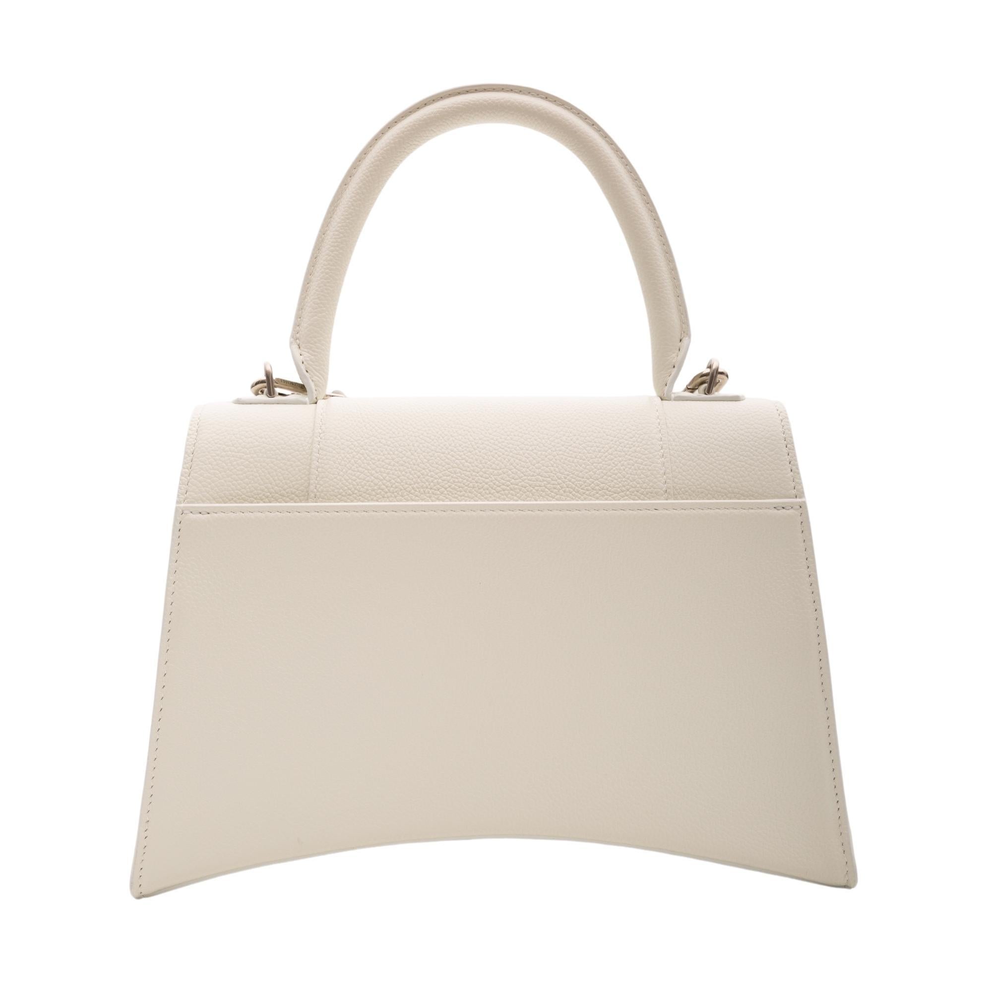 This handbag is made of grained calfskin in white. The bag features a rolled leather top handle, an optional shoulder strap, a signature Balenciaga B charm on front flap, silver hardware, a rear slip pocket and a front flap with snap closure that