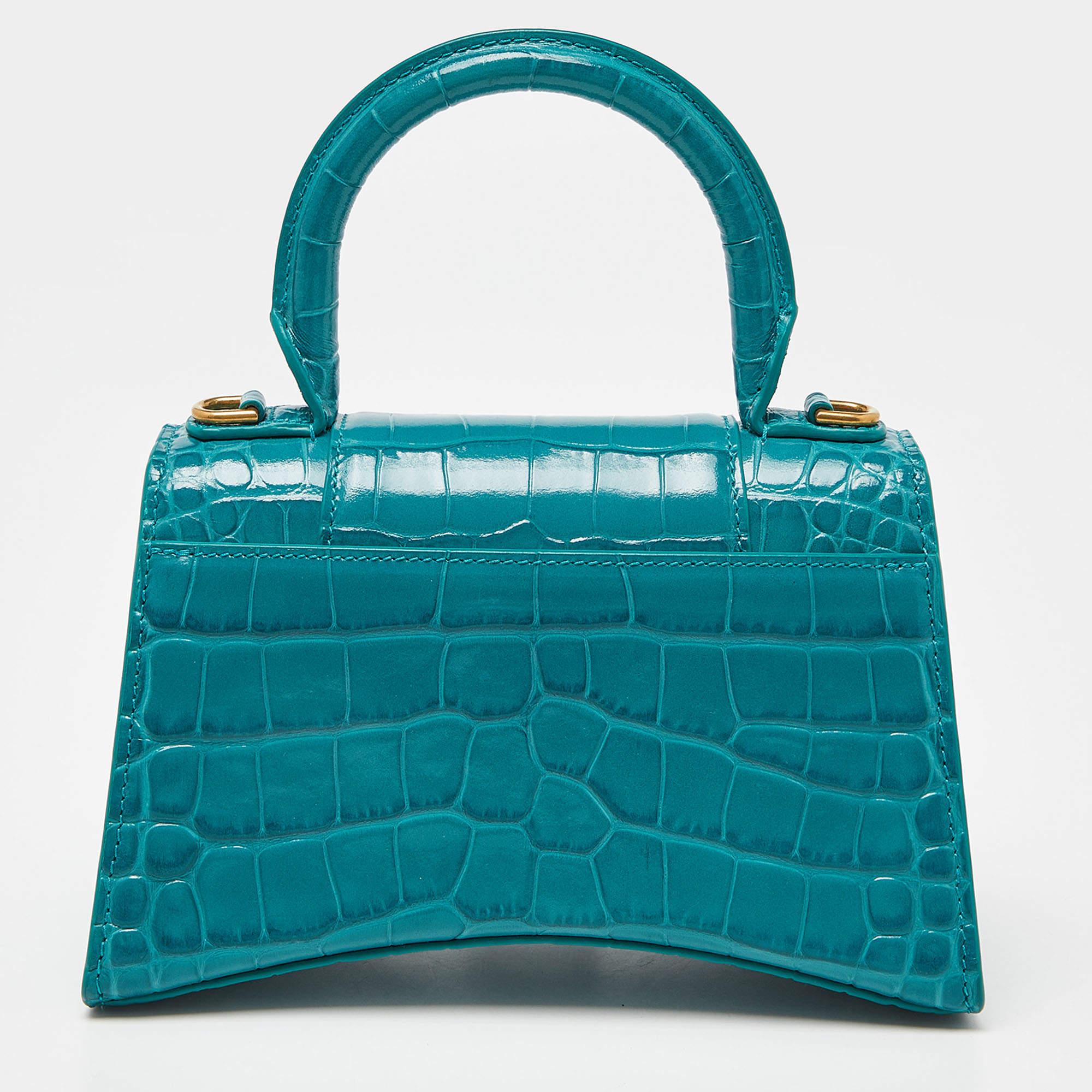The Hourglass features a croc-embossed leather body, a rolled top handle, a detachable flat leather shoulder strap, a front flap with magnetic snap closure, and a spacious interior.

Includes: Original Dustbag, Info Booklet, Detachable Strap