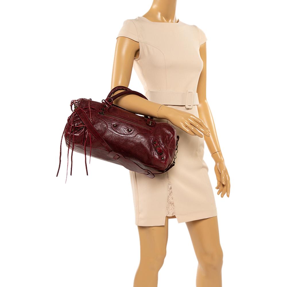 This Balenciaga RH Twiggy Satchel is perfect for everyday use. Crafted from leather in a striking red, this bag has a girlish silhouette with two top handles, a removable shoulder strap, and bronze-tone hardware. The zipper closure opens to a