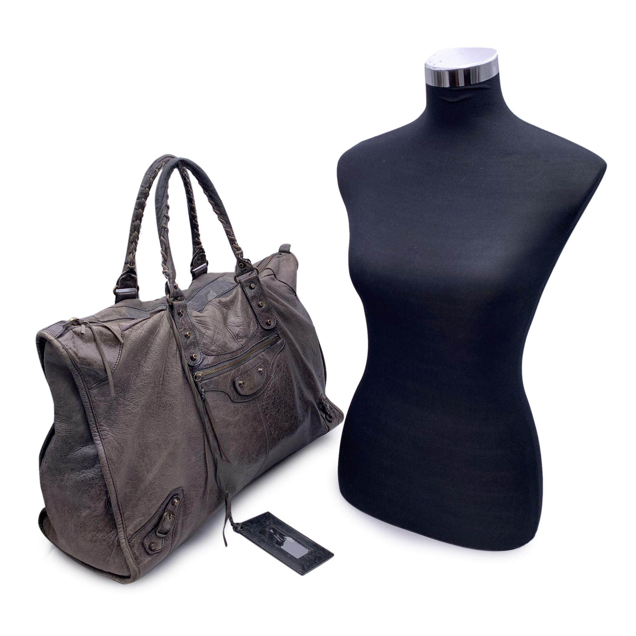 Elegant sac de week-end Balenciaga Classic City XL en cuir gris vieilli. Quincaillerie en métal laiton vieilli . Poignées doubles roulées. Fermeture à glissière sur le dessus. 1 poche zippée sur le devant. Miroir cosmétique assorti inclus. Boucle