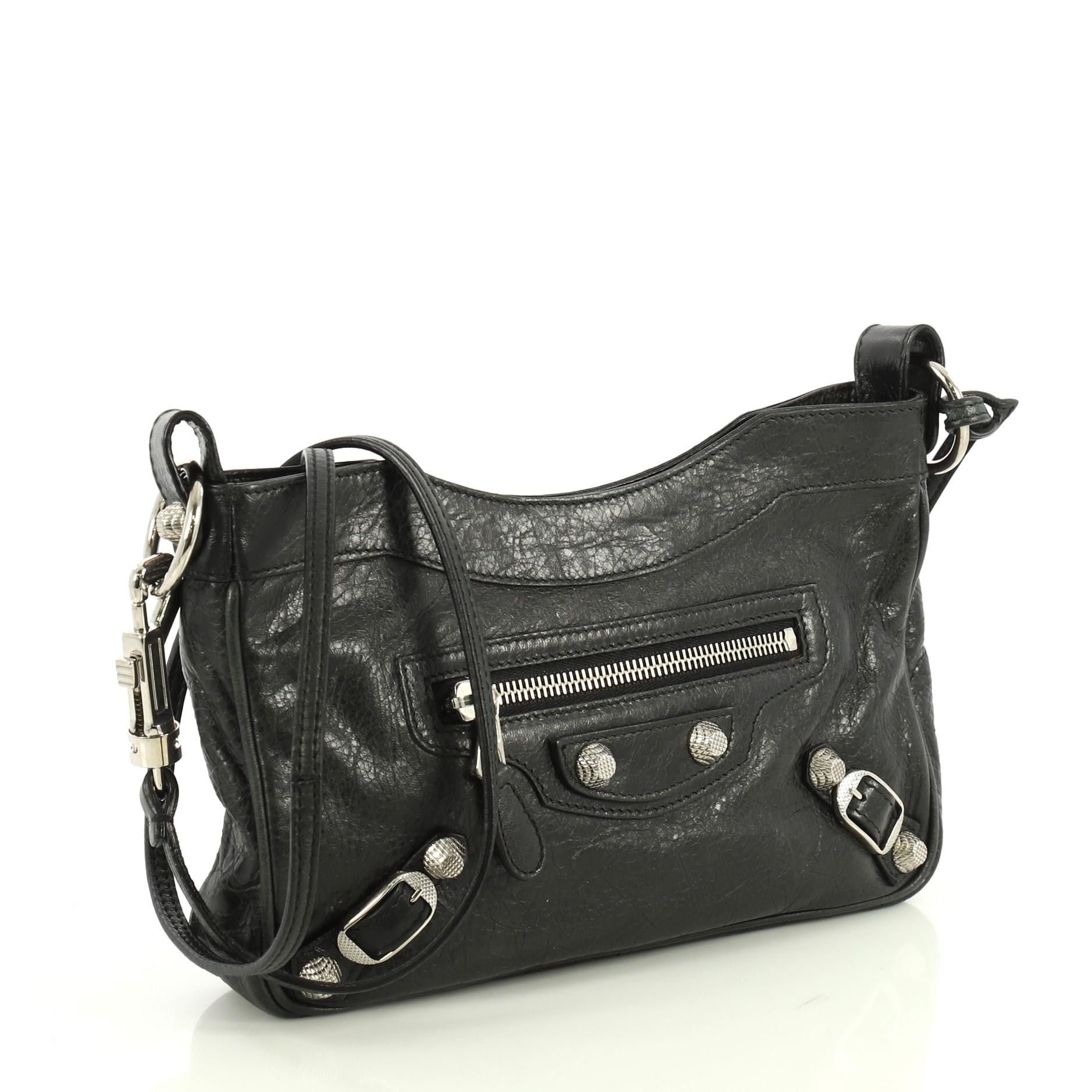 This Balenciaga Hip Giant Studs Crossbody Bag Leather, crafted from black leather, features a long adjustable leather strap, front zip pocket, giant studs and buckle details, and silver-tone hardware. Its top zip closure opens to a black fabric