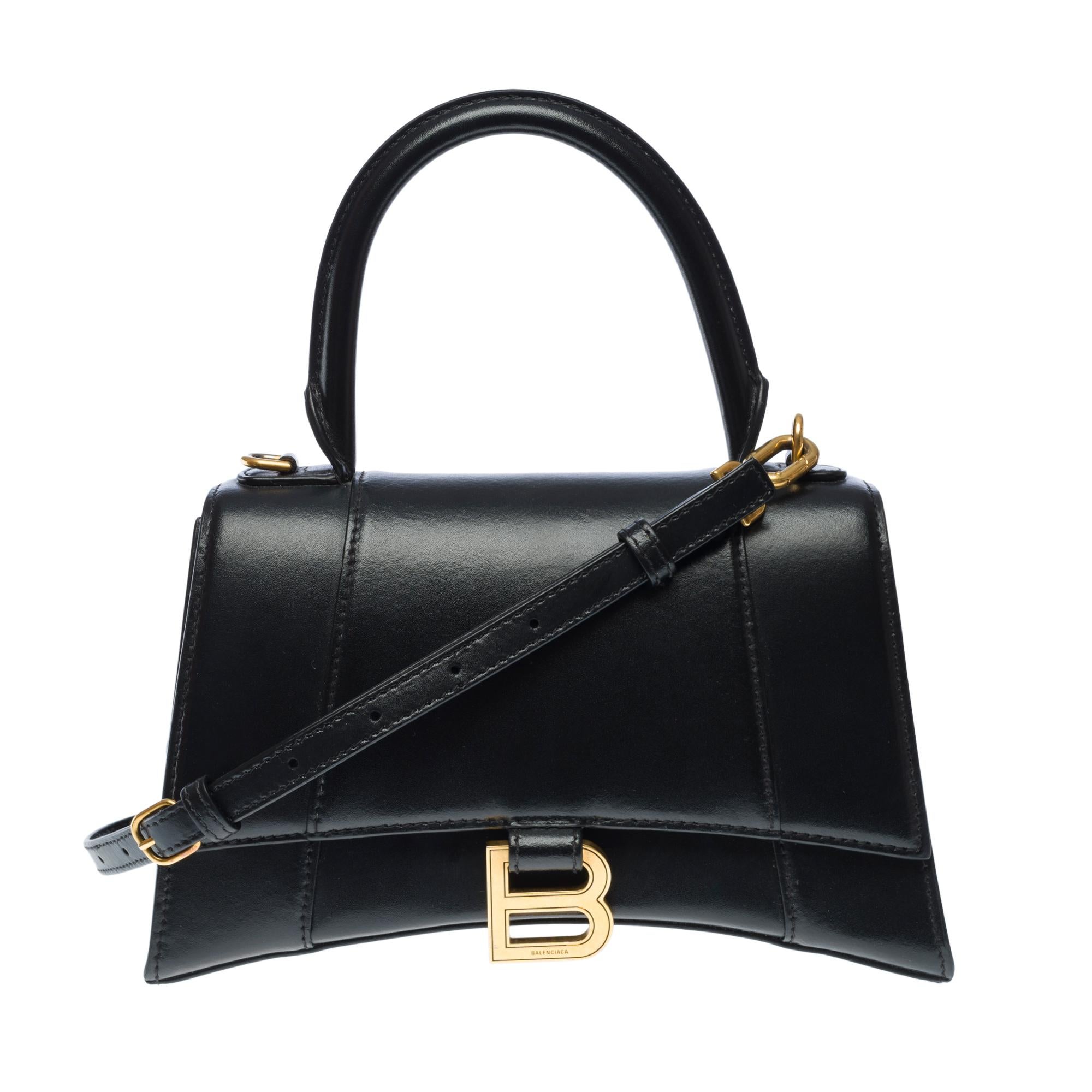 Elegant​ ​Balenciaga​ ​Hourglass​ ​Small​ ​Box​ ​handbag​ ​strap​ ​in​ ​black​ ​box​ ​calfskin​ ​leather,​ ​with​ ​aged​ ​gold​ ​trim​ ​(brass),​ ​a​ ​single​ ​black​ ​leather​ ​handle,​ ​and​ ​a​ ​removable​ ​and​ ​adjustable​ ​shoulder​ ​strap​