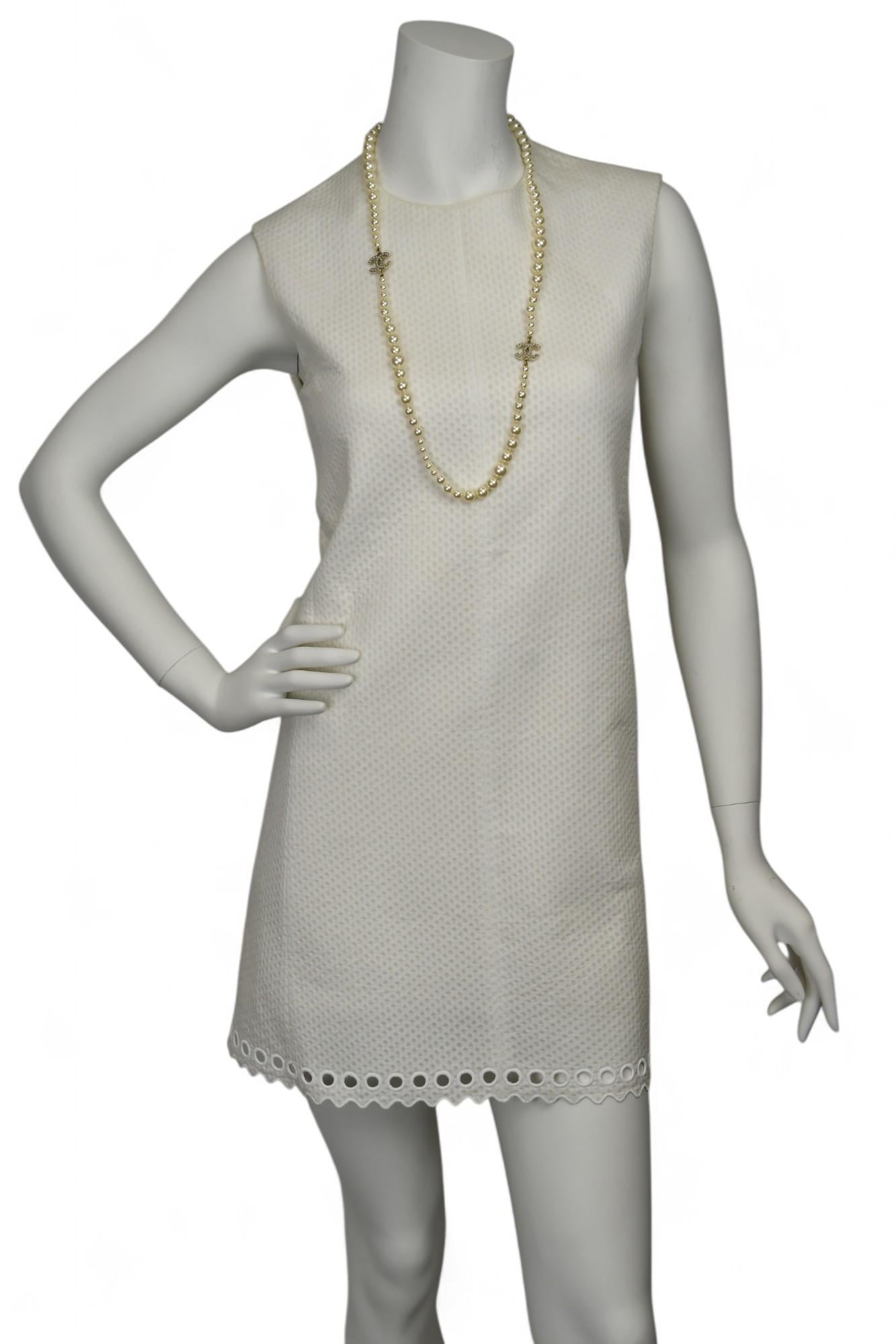 This Balenciaga sleeveless mini dress features a structured silhouette in ivory textured fabric, finished with a charming scalloped eyelet hem. The clean lines, minimalist design, and subtle detailing embody modern elegance with a playful touch.