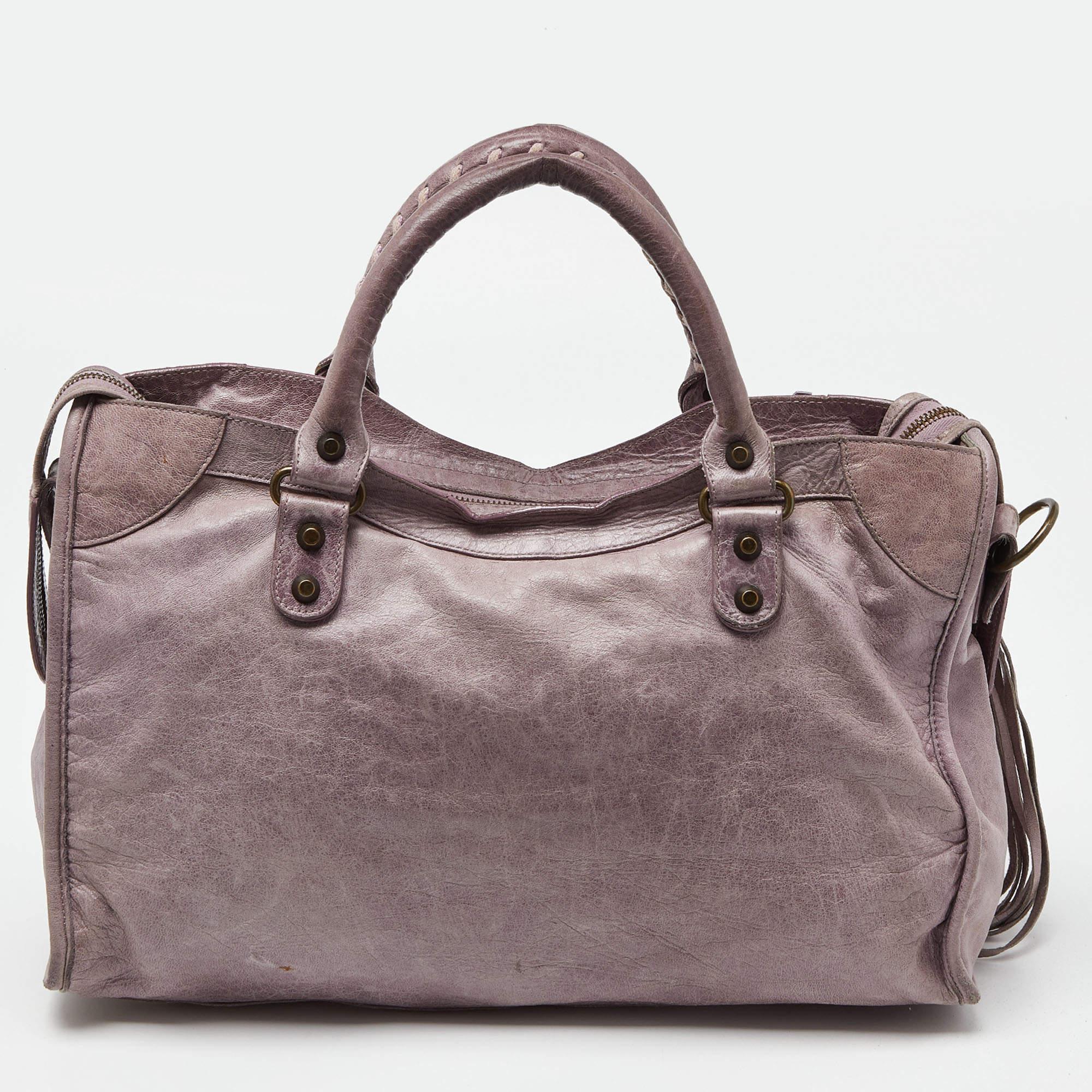 The lilac exterior of this Balenciaga City bag is made chic and highly fashionable with brass-tone accents. Crafted from leather, it is equipped with a front zipper pocket and can be carried with dual handles. The fabric-lined interior is perfectly