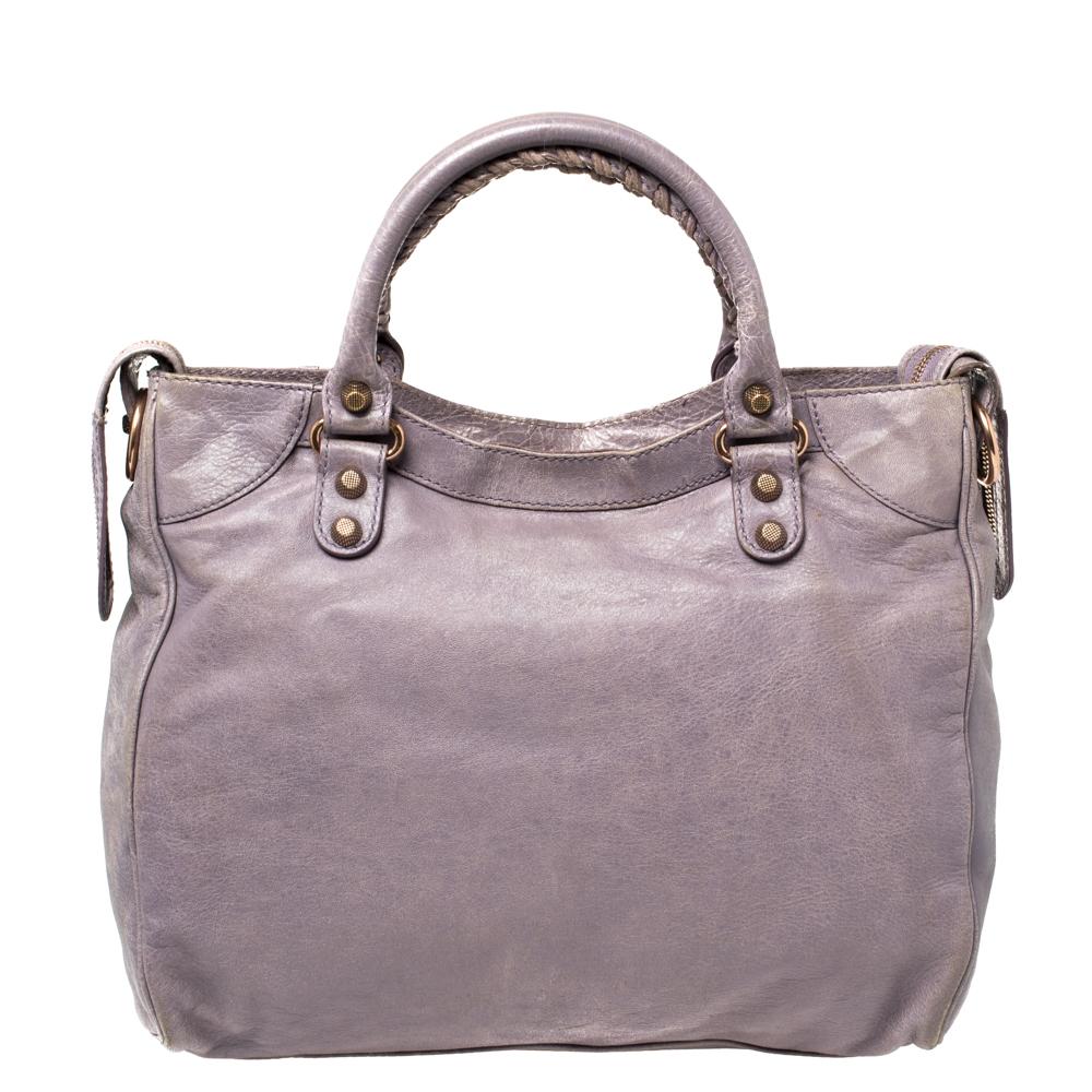 Crafted using leather, this RH Velo tote from Balenciaga comes in a trendy lilac hue, complemented by rose gold-tone hardware. The tote has two handles, studs, buckles, a detachable mirror, and a spacious fabric interior.

Includes: Mirror, Strap,