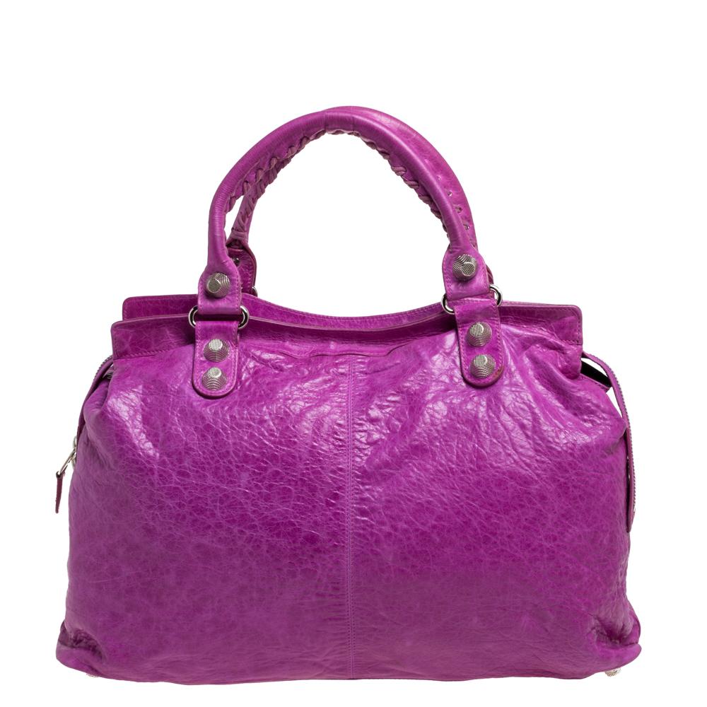 This Balenciaga RTT bag is perfect for everyday use. Crafted from leather in a gorgeous magenta hue, the bag has a feminine silhouette with two top handles and silver-tone hardware. The zipper closure opens to a fabric-lined interior and the bag is