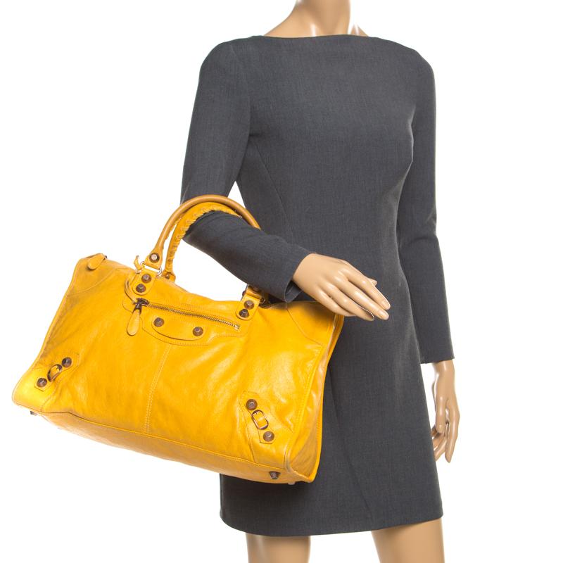 This Balenciaga work tote is a perfect blend of urbanity and style. The signature studs made from gold hardware adorns the front exterior with added buckle accents in the corner. The bag profiles dual handles along with a front zip pocket sitting on