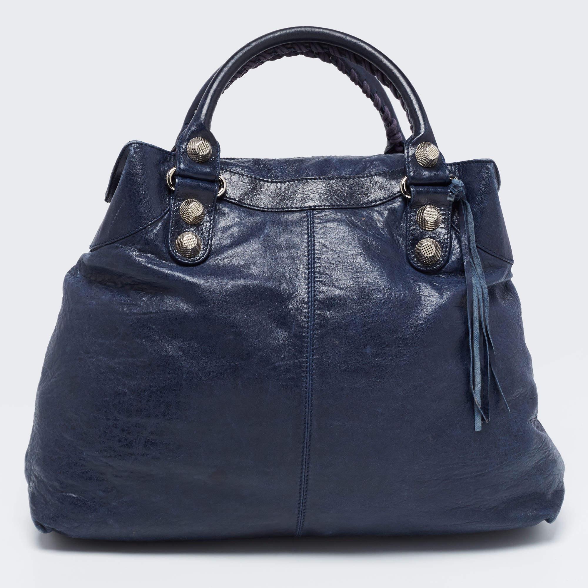 Quite popular bag among celebrities, this GSH Brief tote by Balenciaga will never leave you unnoticed! It is crafted from marine leather and is accented with oversized signature metal buckle and stud details at the front. It comes with an exterior