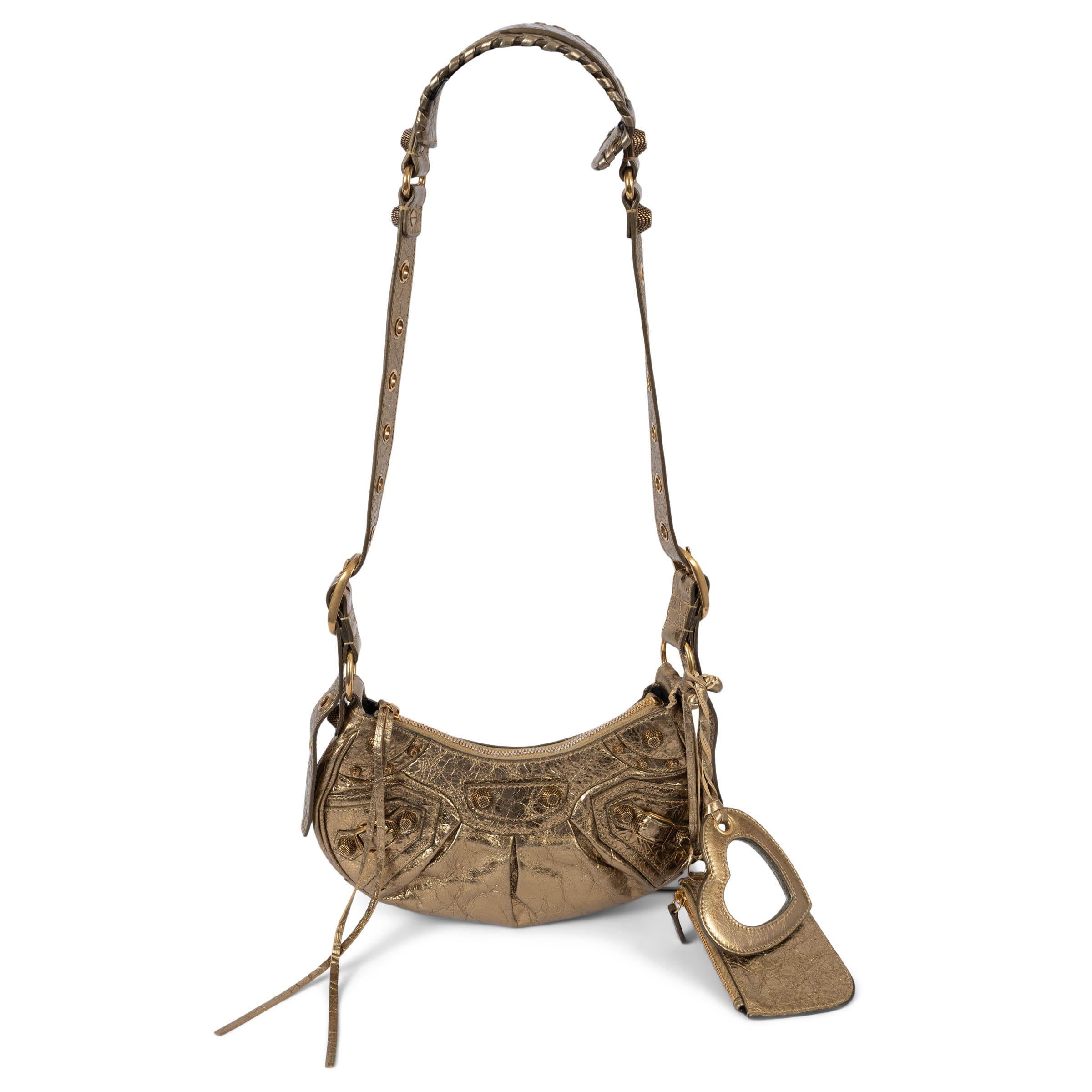 100% authentic Balenciaga Le Cagole XS shoulder bag in cracked metallic gold Aren lambskin leather. The bag opens with a top zipper and is lined in black canvas. and is adorned with numerous buckles and textured conical studs inspired by the moto