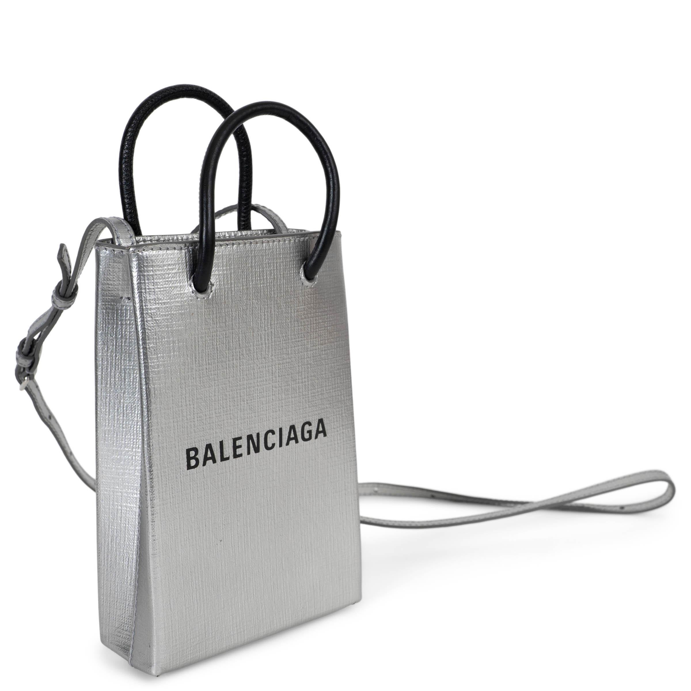 Cette pochette de téléphone Mini Shopping Tote 100% authentique de Balenciaga est réalisée en cuir argenté métallisé. Il est doté de deux poignées tubulaires en cuir d'agneau noir et d'un logo Balenciaga noir contrasté sur le devant. Une sangle