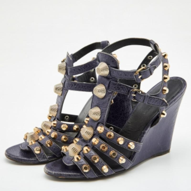 These stunning sandals by Balenciaga will make a statement. Crafted from leather, they come in navy blue. These gladiator-style wedge heels feature straps embellished with gold-tone studs, buckle closure, 11.5 cm heels, and robust soles. They are