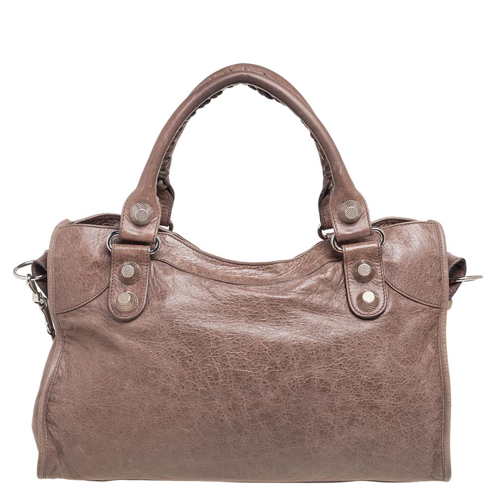 Crafted from luxurious leather, this Balenciaga bag is an easy match with most outfits. Its distinctive feature is the bold studs & buckled and has rolled, top handles. The front zipped pocket, framed leather mirror, and a roomy interior make this