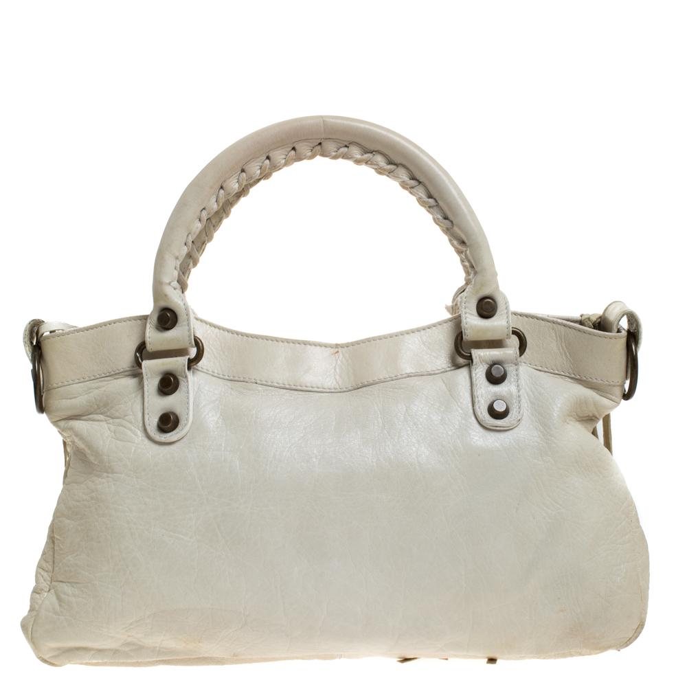 This Balenciaga RH First bag is crafted from leather in a gorgeous off-white hue, the bag has a feminine silhouette with two top handles and bronze-tone hardware. The zipper closure opens to a fabric-lined interior and the bag is enhanced with