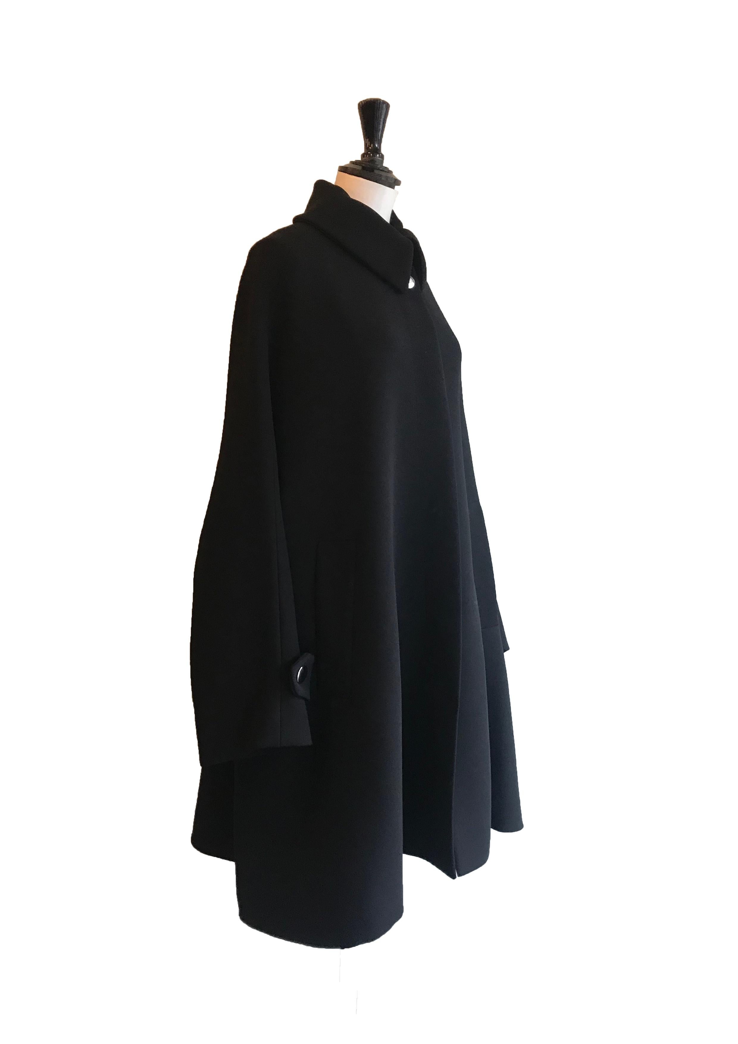Black Opera style coat from Balenciaga. Triangular, oversized, cape like shape. Invisible popper fastening with statement silver stud button at the collar. Diagonal slip pockets either side of hip. Wide, dropped style sleeves with flap detail