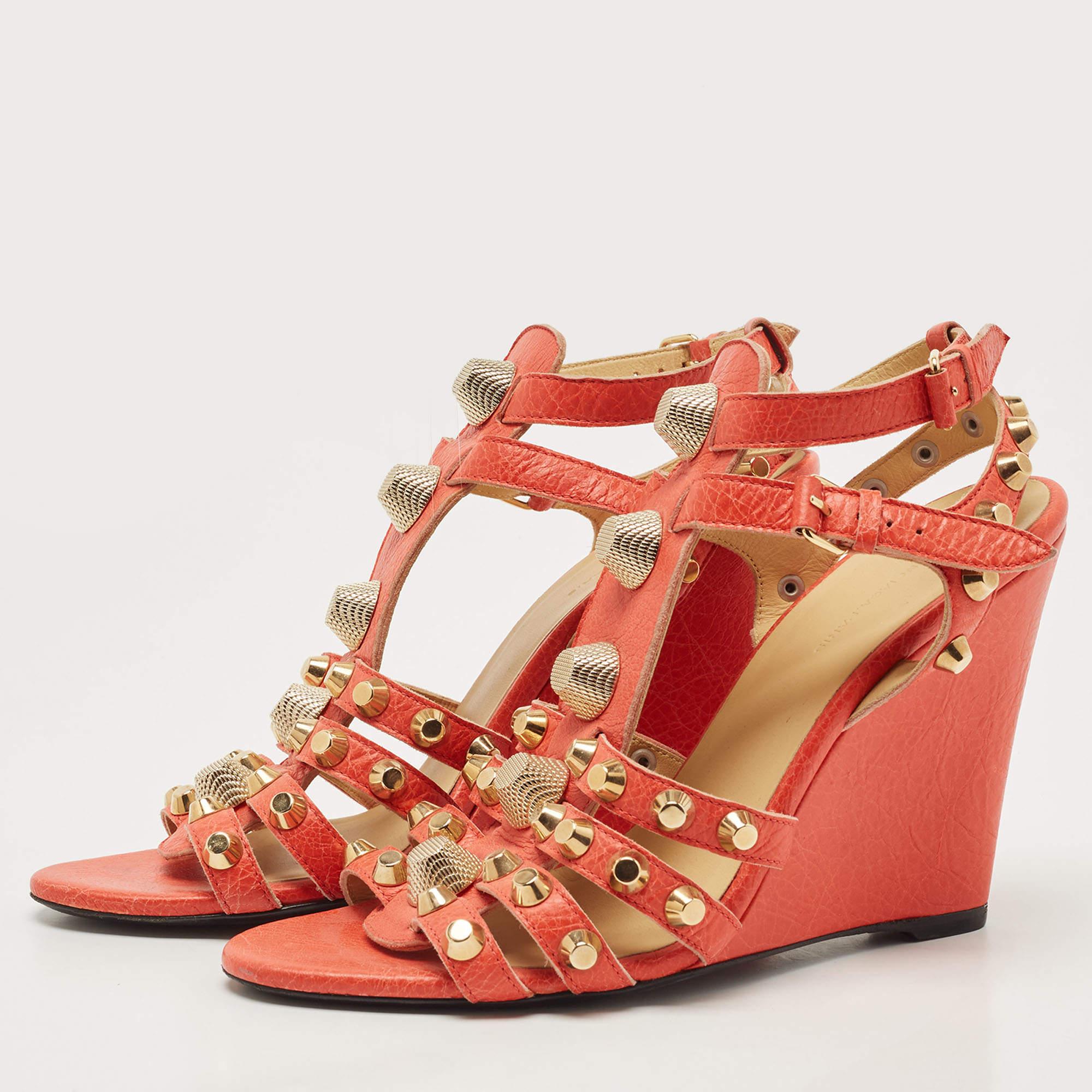 An orange shade, neat stitching, and stud details define this pair by Balenciaga. The sandals are crafted from leather and feature open toes, buckle fastening, and wedge heels.


