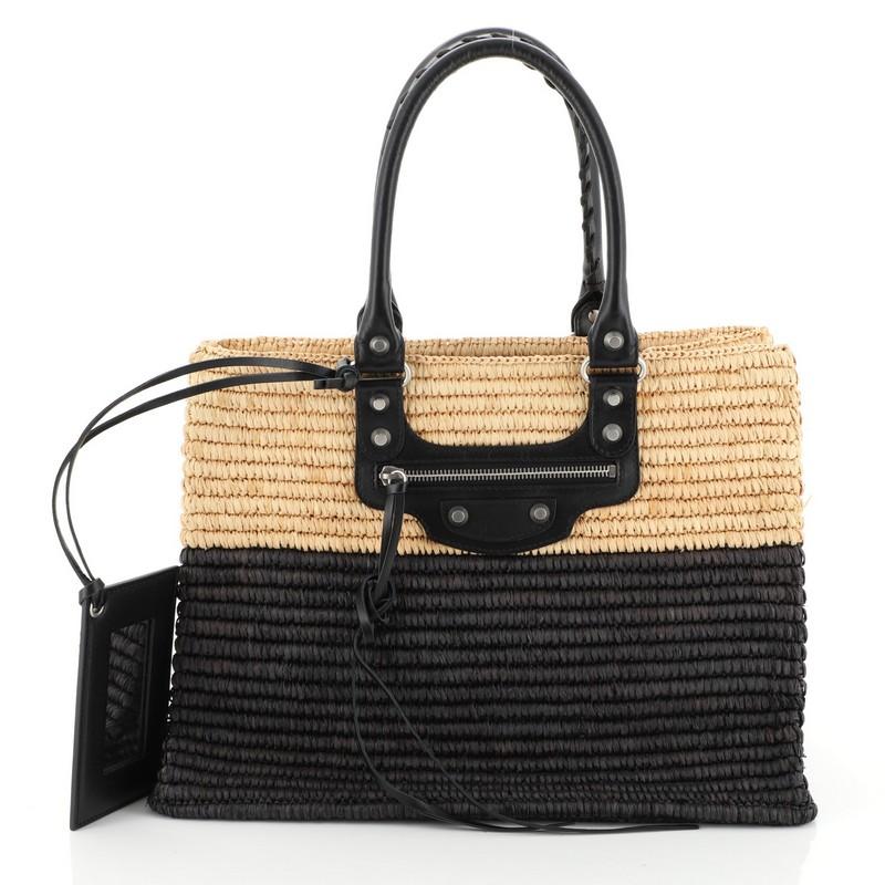 This Balenciaga Panier Shopping Tote Woven Raffia XS, crafted in black and neutral woven raffia, features dual-rolled braided handles, front zip pocket, iconic Balenciaga classic studs, and buckle details and matte silver-tone hardware. Its wide