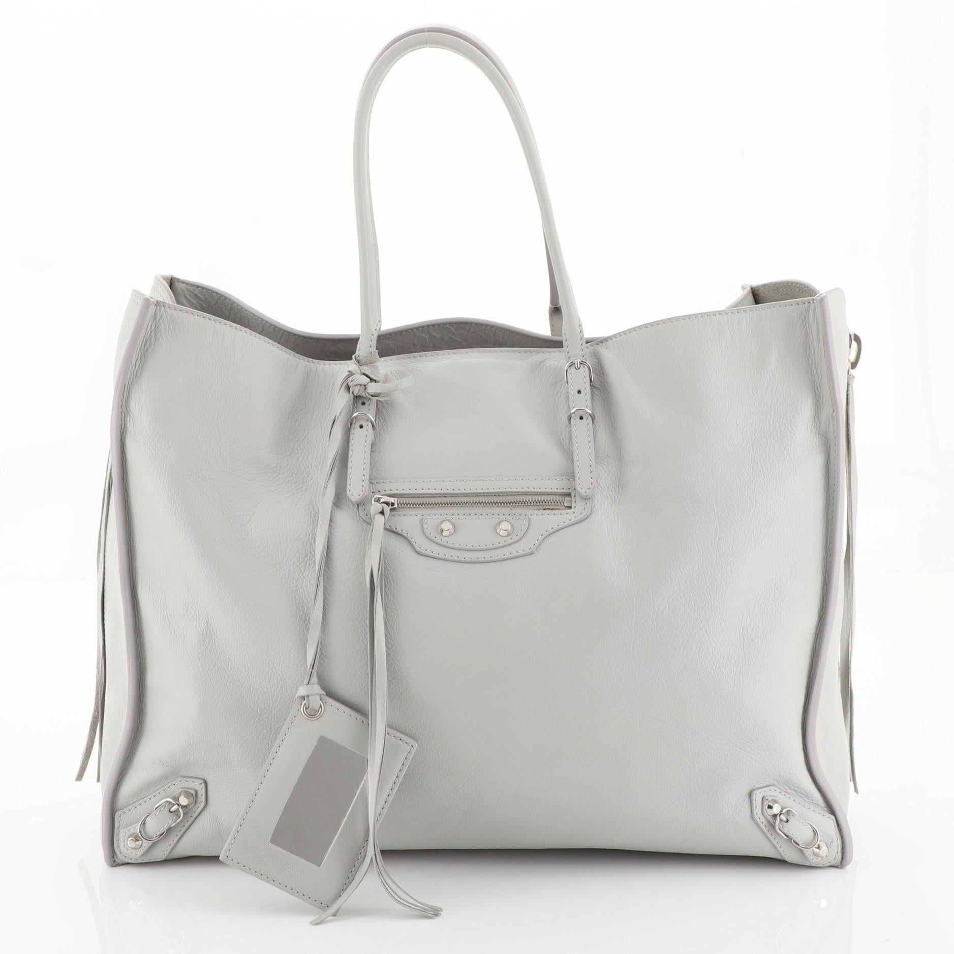 This Balenciaga Papier A4 Zip Around Classic Studs Bag Leather Large, crafted in gray leather, features dual slim handles, front zip pocket, studs and buckle details, and silver-tone hardware. It opens to a gray leather and suede interior with slip