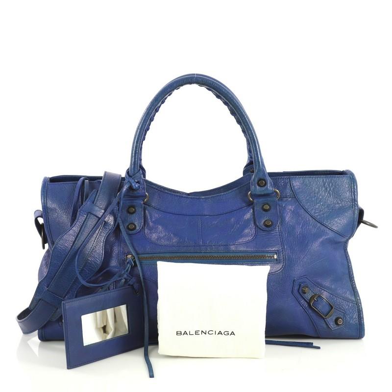 This Balenciaga Part Time Classic Studs Bag Leather, crafted from blue leather, features dual braided woven handles, classic studs and buckle details, front zip pocket, and antique brass-tone hardware. Its top zip closure opens to a black fabric