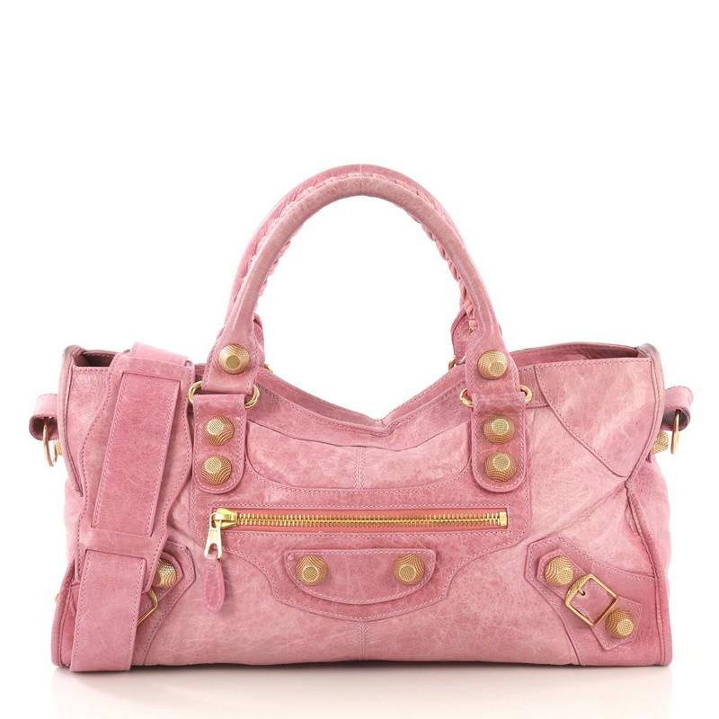 This Balenciaga Part Time Giant Studs Bag Leather, crafted in pink leather, features front zip pocket, dual rolled braided handles, giant studs and buckle details, and gold-tone hardware. Its top zip closure opens to black fabric interior with zip
