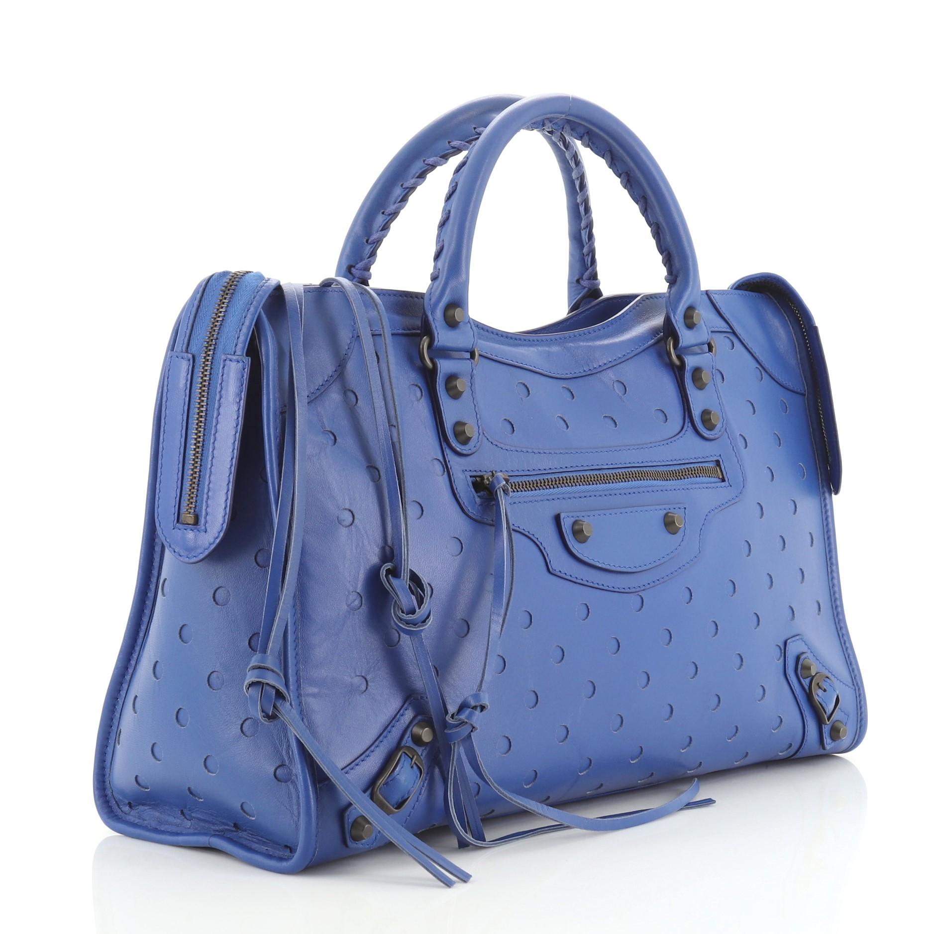 This Balenciaga Polka Dot City Classic Studs Bag Perforated Leather Medium, crafted in blue leather, features perforated polka dots design, braided woven handles, long fringe detailing, front zip pocket, classic studs and buckle details, and