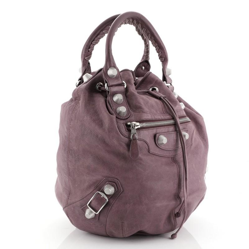 This Balenciaga Pom Pon Giant Studs Handbag Leather, crafted in purple leather, features braided top handles, buckle and stud detailing, and silver-tone hardware. Its drawstring closure opens to a black fabric interior with a side zip pocket.