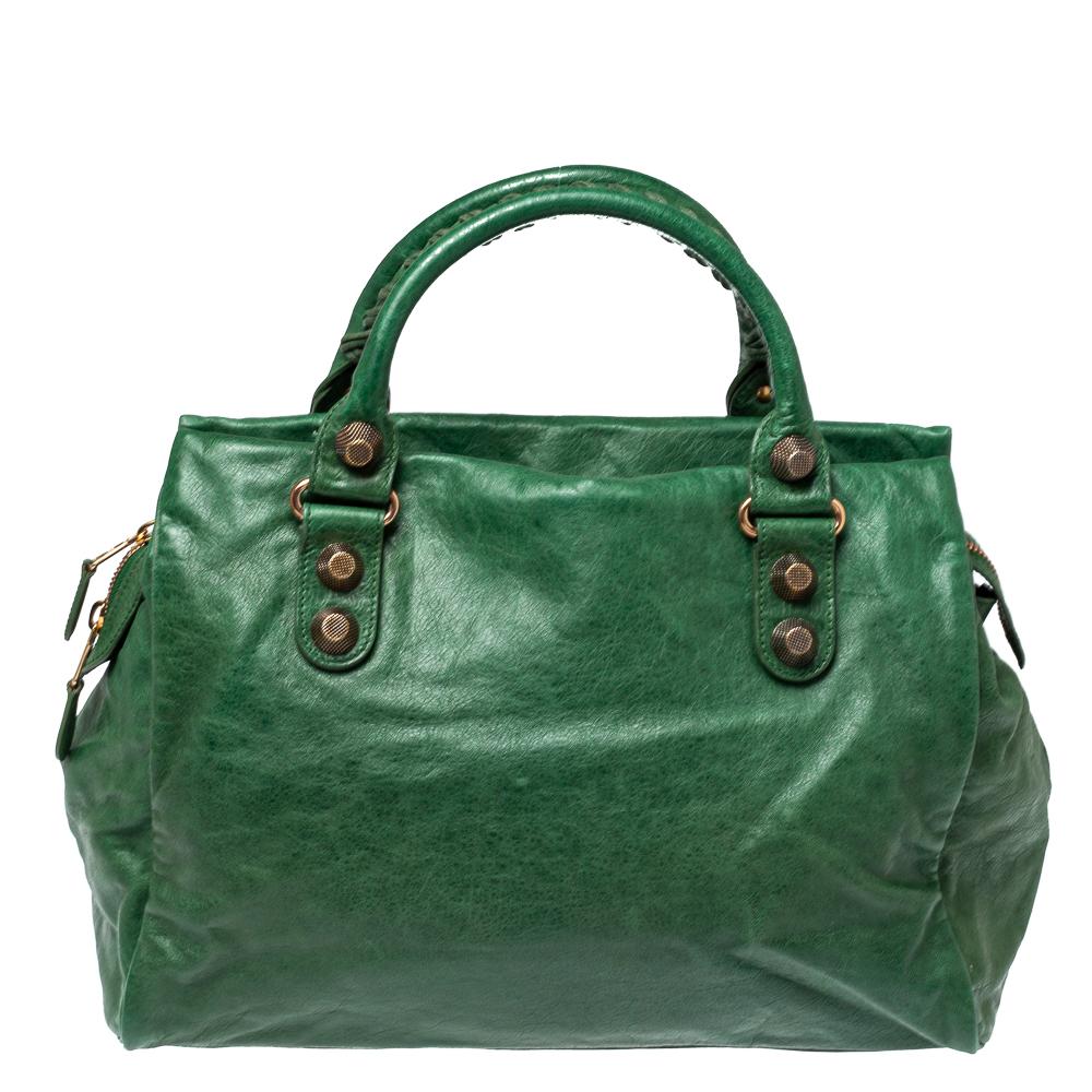 This Midday tote by Balenciaga will be a handy companion! It is crafted from leather and is accented with signature metal buckle and stud details on the front. It comes with an exterior zip pocket and dual top handles. A spacious fabric-lined