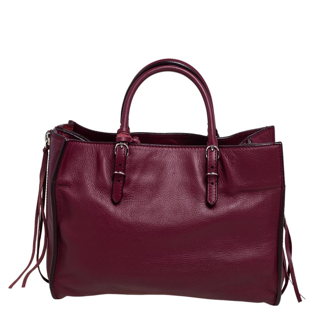 Papier A6 tote from Balenciaga smoothly blends luxury with practical fashion. It comes crafted from Pourpre Veau leather into a structured body and styled with two top handles and a spacious interior. But it is the zippers and buckle detailing which