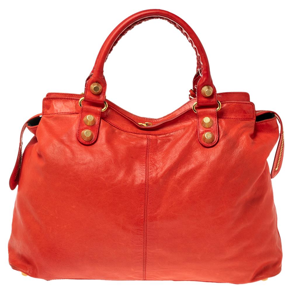This Balenciaga RTT bag is perfect for everyday use. Crafted from leather in a gorgeous red hue, the bag has a feminine silhouette with two top handles and gold-tone hardware. The zipper closure opens to a fabric-lined interior and the bag is