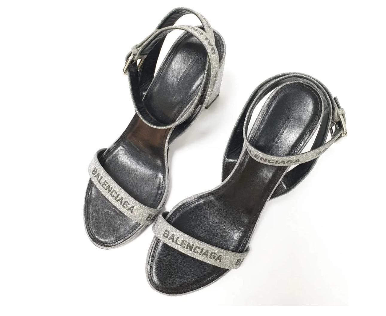 Gehen Sie stilvoll aus mit diesen Balenciaga Sandalen mit rundem Glitzerlogo! Diese auffälligen Sandalen haben ein glitzerndes Obermaterial und ein Futter aus Kalbsleder, das sowohl Stil als auch Komfort garantiert. Das kultige Balenciaga-Logo