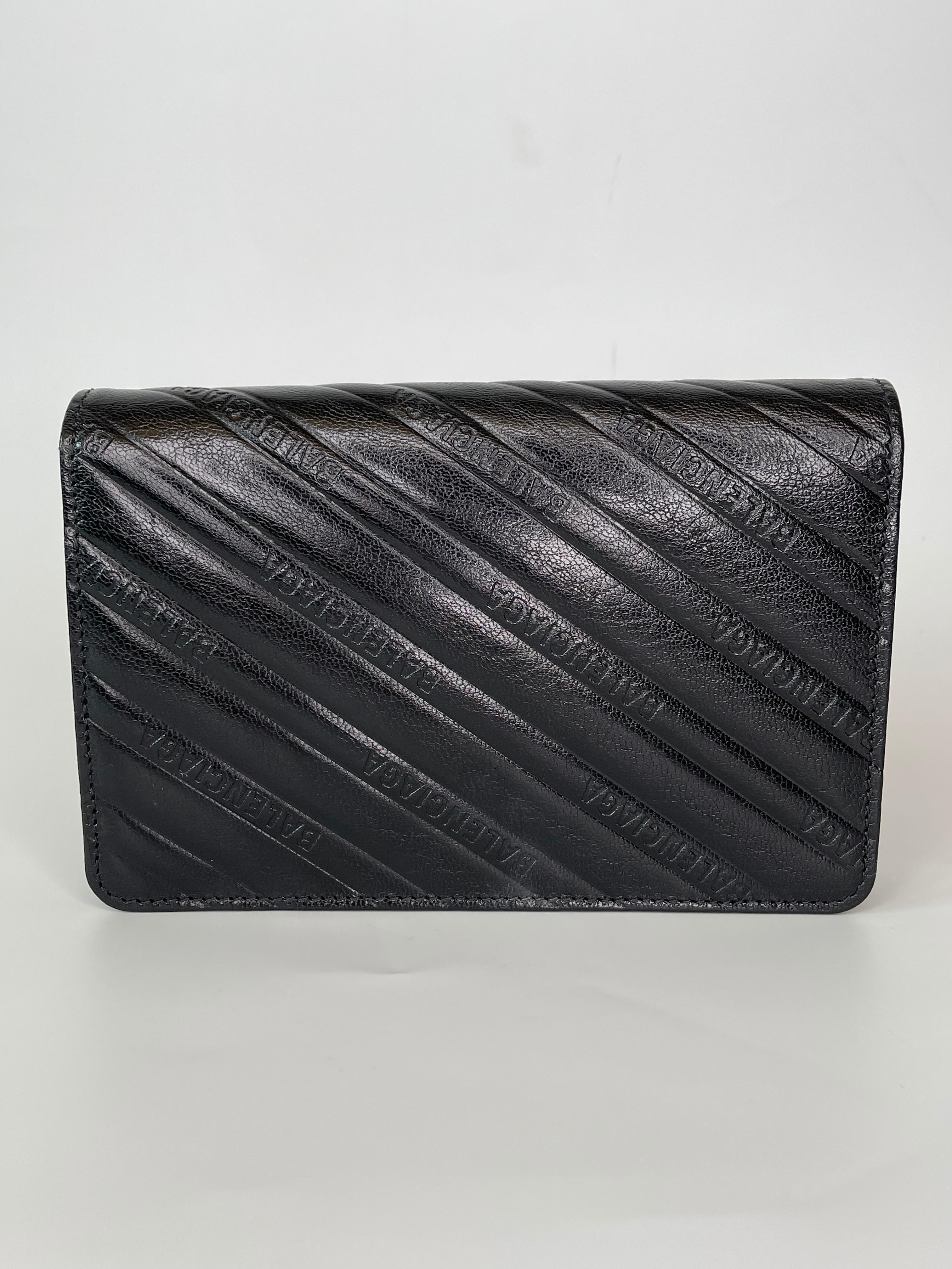 This WOC bag is made with crinkled goatskin leather in black with “Balenciaga” embossed throughout the surface. The bag features an aged gold chain link shoulder strap, and a matching Balenciaga BB logo on the crossover flap. The bag opens with a