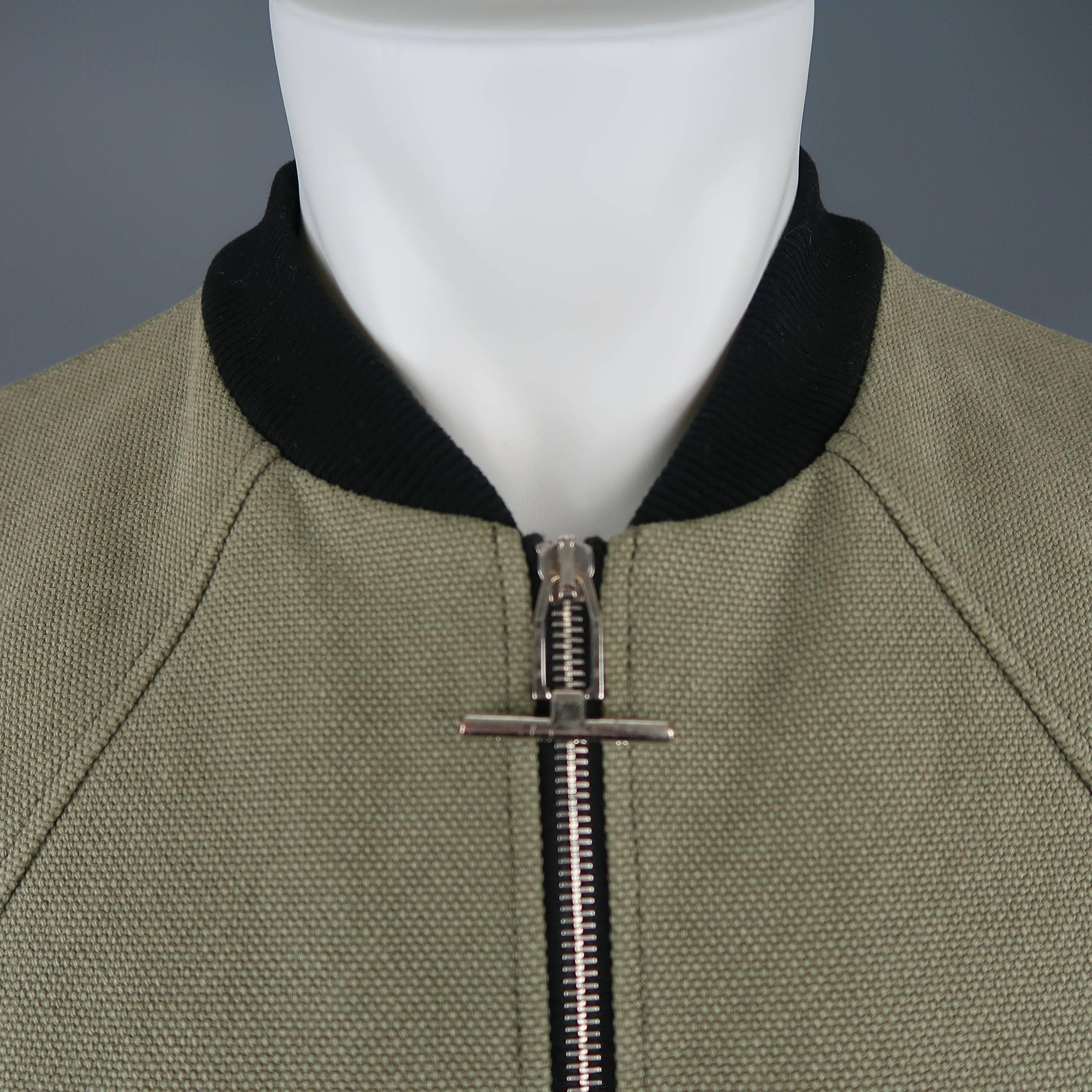 BALENCIAGA by ALEXANDER WANG Cristóbal cropped bomber jacket comes in olive green canvas with curved raglan sleeves, zip front with silver tone engraved tab, black ribbed baseball collar and cuffs, and extended back. Minor wear and small