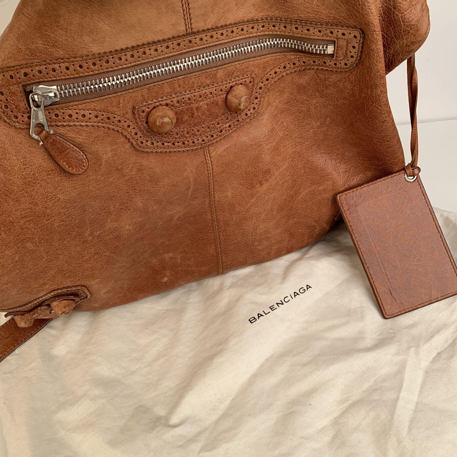 - Balenciaga 'Giant Besace' Hobo Bag
- Crafted in tan leather with brogues perforated trim
- Buckle detailing on bottom corners and decorative covered studs
- 1 front zip pocket
- Open top
- Black fabric interior
- 1 side zip pocket inside
-