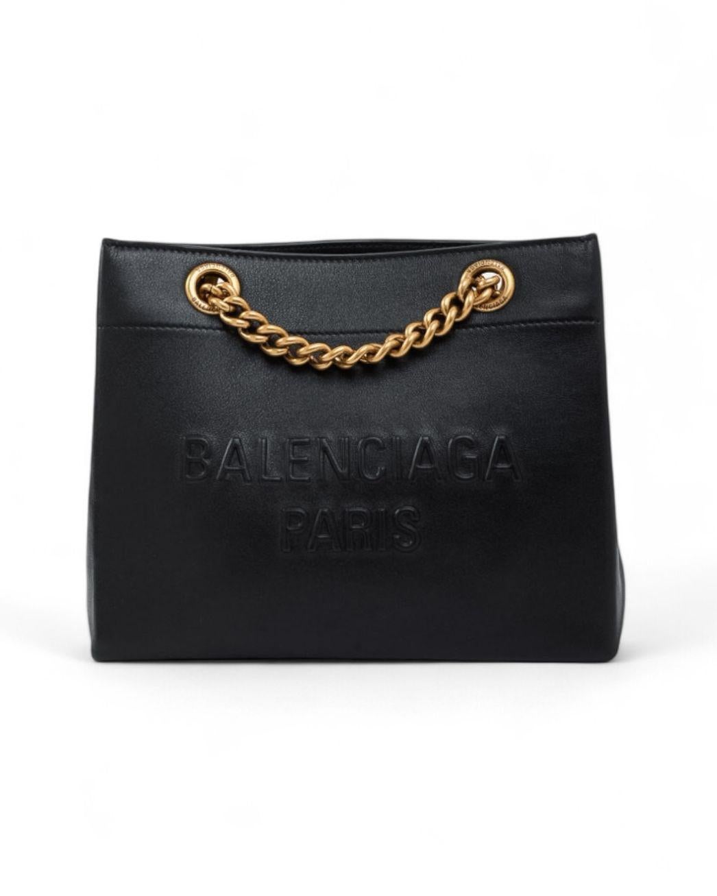 Bolso Balenciaga, modelo Tote Duty Free, talla Small, realizado en piel negra lisa con detalles de herrajes dorados. El modelo no tiene cierre, lo que le confiere un diseño abierto y versátil. El interior, forrado en lona de algodón tono sobre tono,