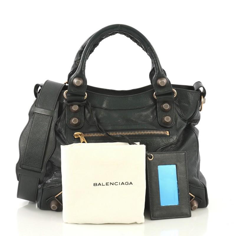 This Balenciaga Velo Giant Studs Bag Leather, crafted from dark green leather, features dual braided handles, signature giant studs and buckle details, exterior front zip pocket, and rose gold-tone hardware. Its top zip closure opens to a black
