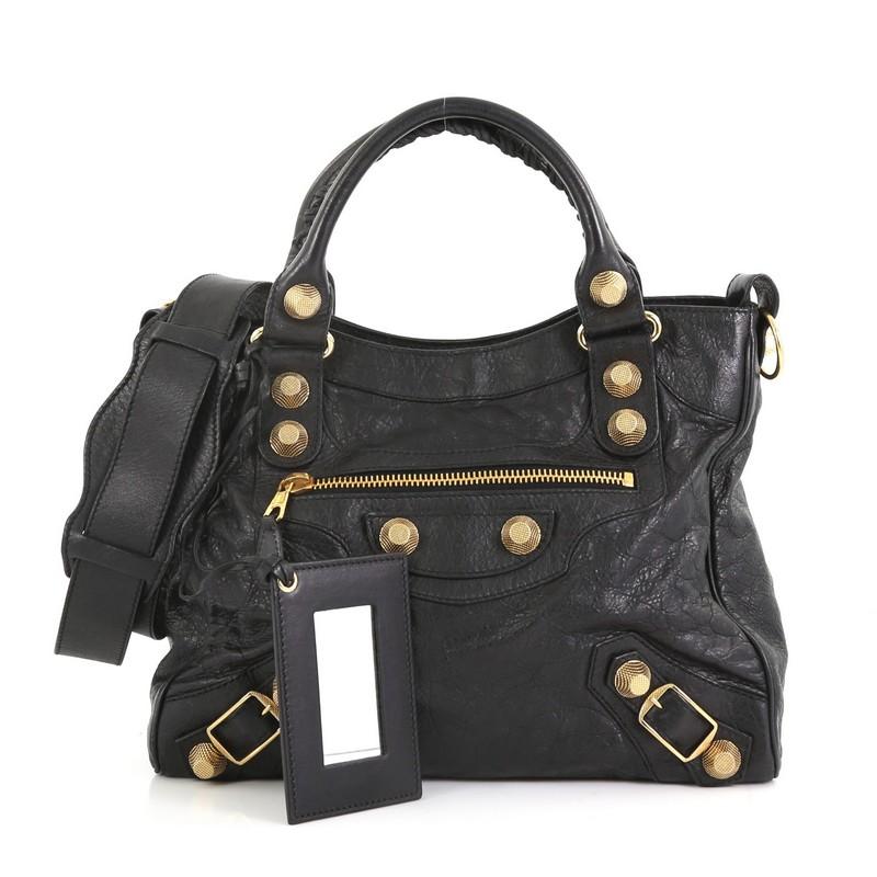 This Balenciaga Velo Giant Studs Bag Leather, crafted from black leather, features dual braided handles, signature giant studs and buckle details, exterior front zip pocket, and gold-tone hardware. Its top zip closure opens to a black fabric