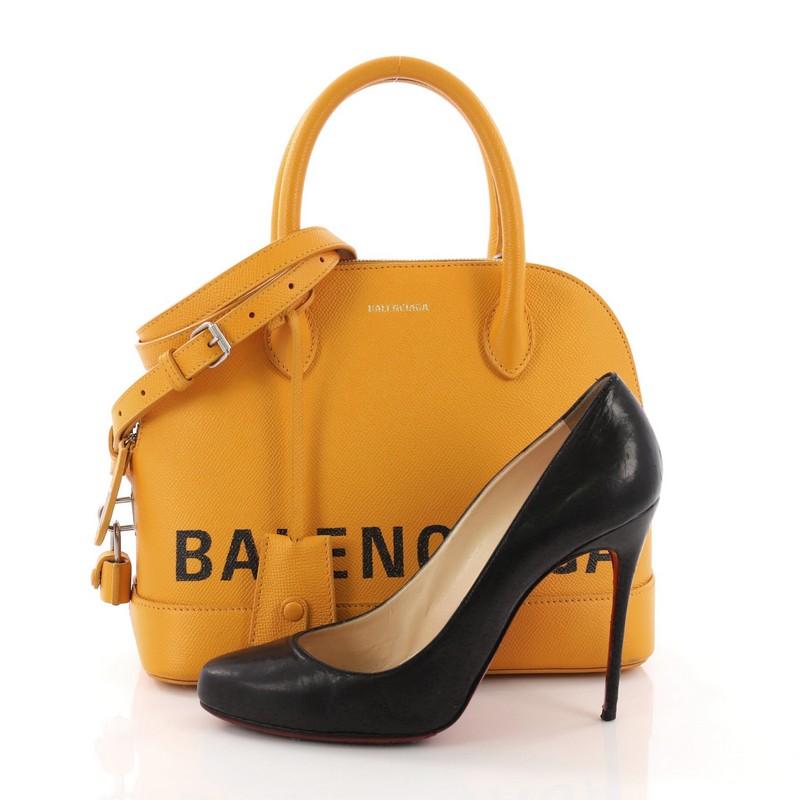 This Balenciaga Ville Logo Bag Leather Small, crafted from yellow leather, features dual rolled leather handles, protective base studs, and silver-tone hardware. Its zip closure opens to a black leather and fabric interior with zip pocket. **Note: