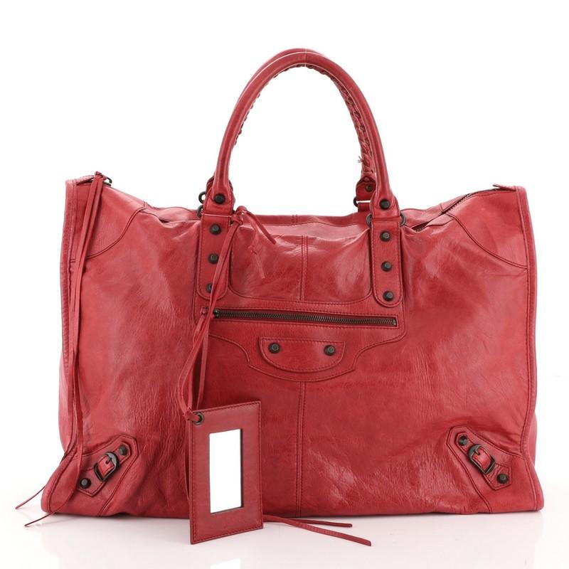 This Balenciaga Weekender Classic Studs Bag Leather, crafted from red leather, features dual braided woven handles, stud and buckle details, exterior front zip pocket, and brass-tone hardware. Its top zip closure opens to a black fabric interior
