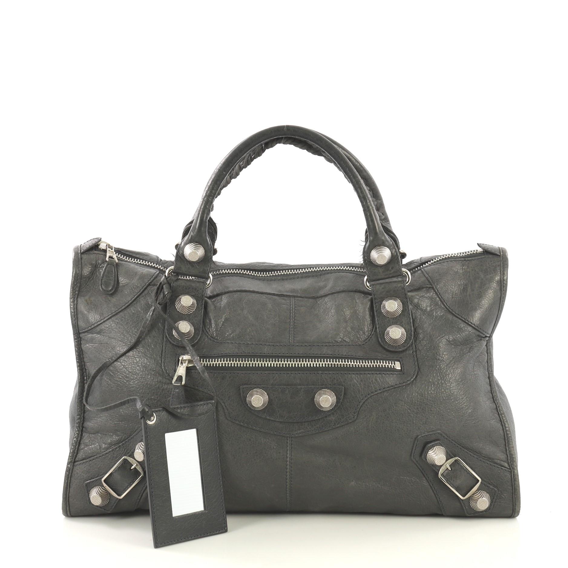 This Balenciaga Work Giant Studs Bag Leather, crafted from grey leather, features dual braided woven handles, exterior front zip pocket, stud detailing, and silver-tone hardware. Its top zip closure opens to a black fabric interior with side zip and