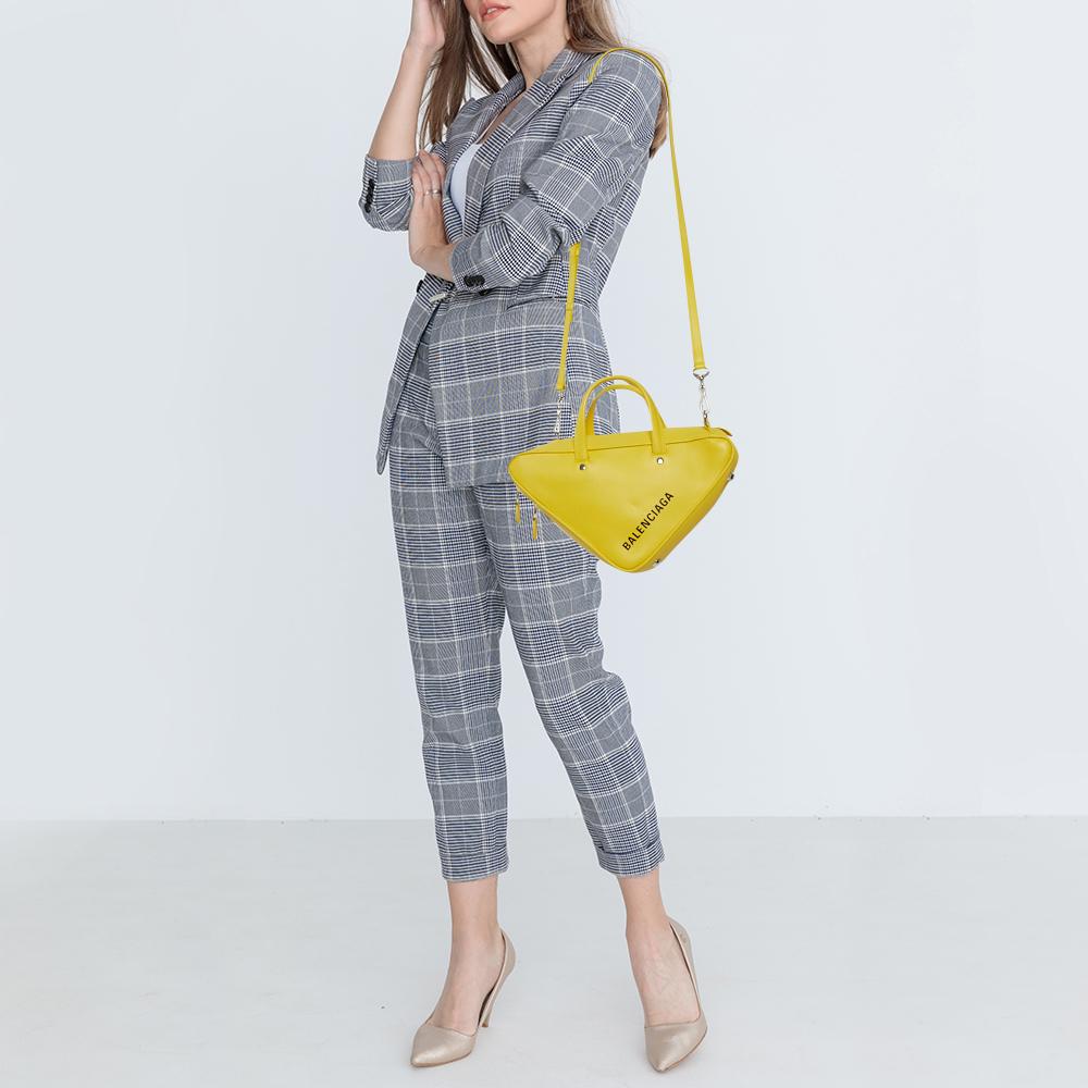 From the house of Balenciaga, this bag is an outstanding fusion of brilliance and style. It has a triangular silhouette and a fresh take on a duffle bag. It is crafted from bright yellow leather and is made in Italy. It comes with dual handles, bold