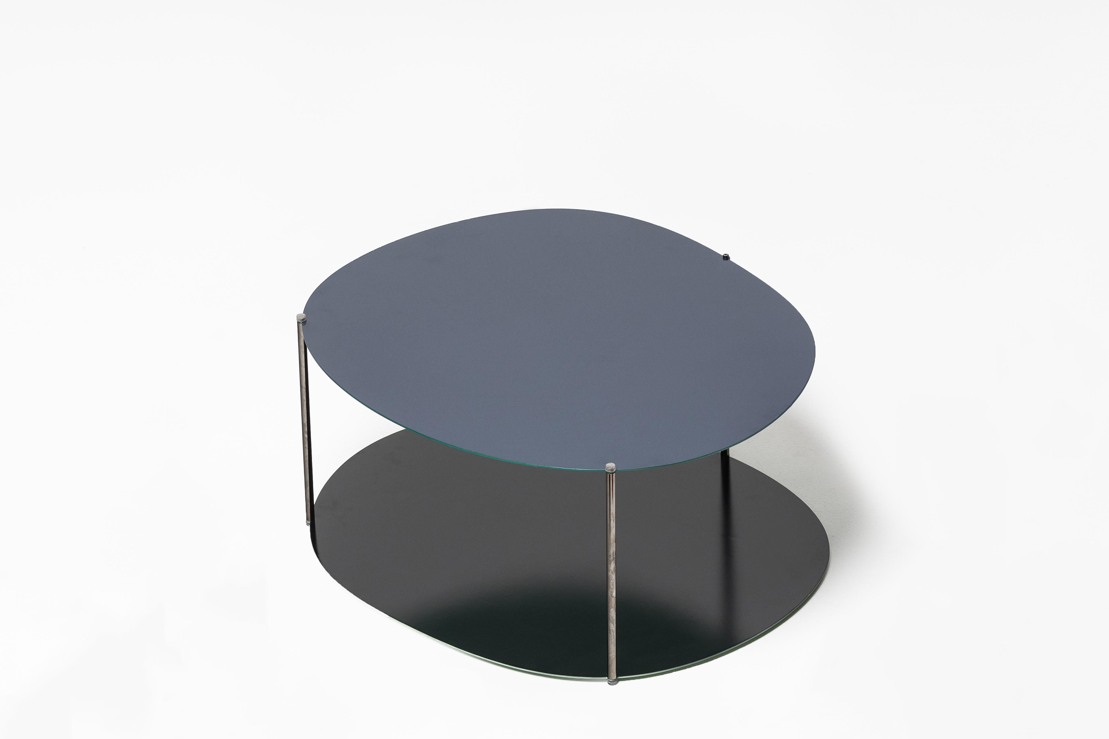Mesa de centro con tableros reversibles de acero de 0,2 cm de grosor y revestimiento líquido en ambas superficies. Las partes superiores están unidas por barras redondas de acero con acabados de cromo negro pulido.

 