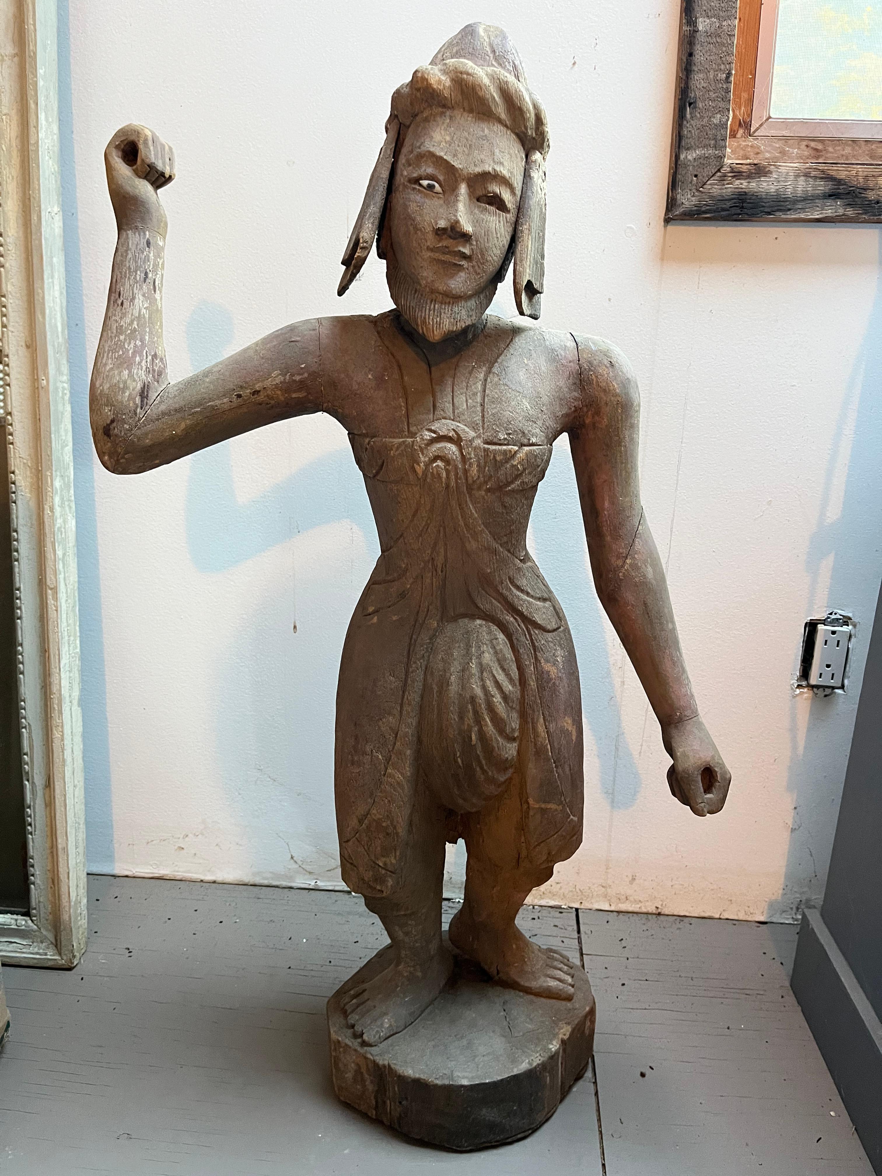 A carved wood statue of a warrior in traditional clothing, late 19th century-early 20th century. Retains traces of its original painted finish.