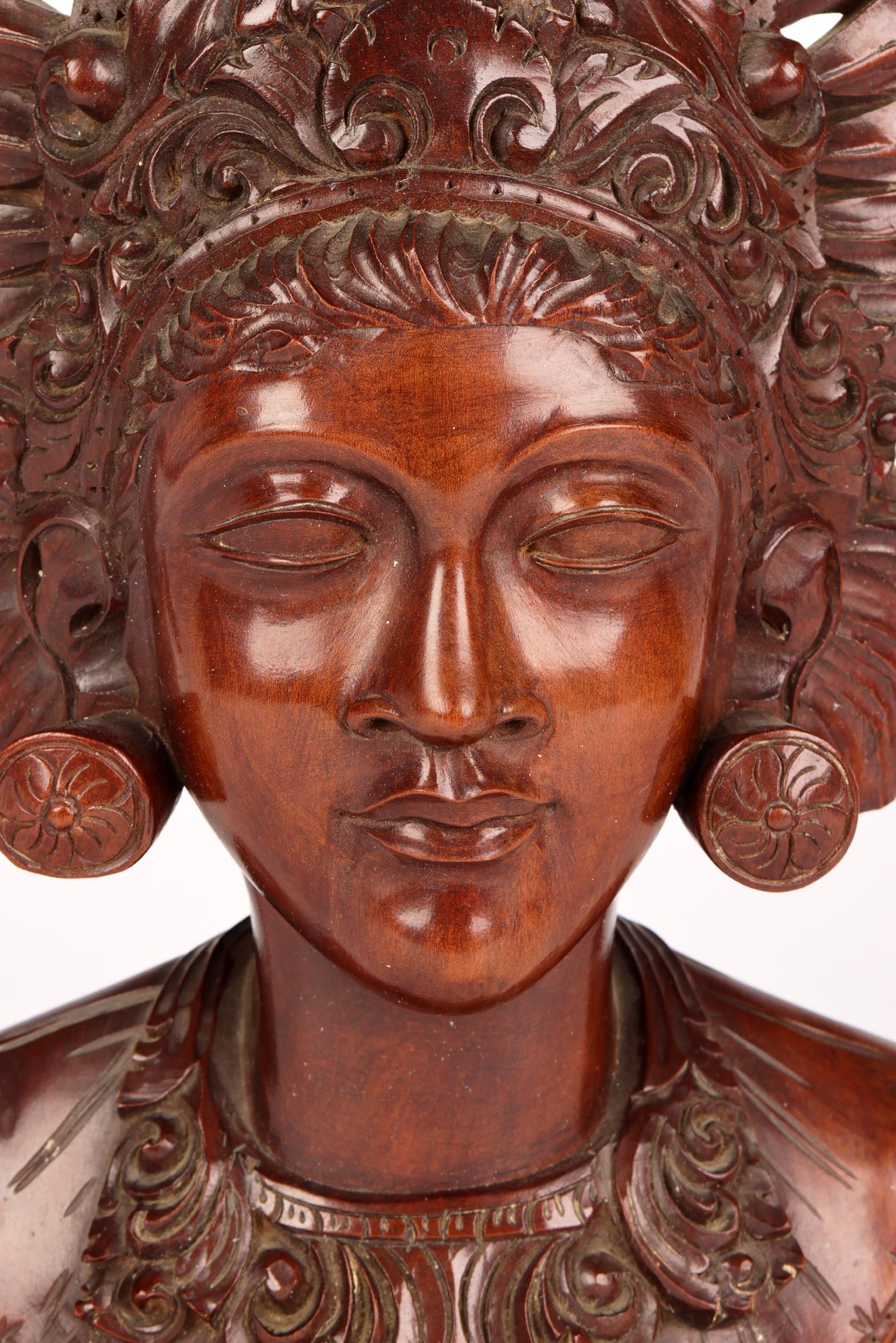 A well carved wooden portrait bust of a young girl wearing an elaborate headdress carved by a Balinese artist around the mid 20th century. The bust is carved from a single piece if wood, possibly sandal wood, and is well carved with good detail
