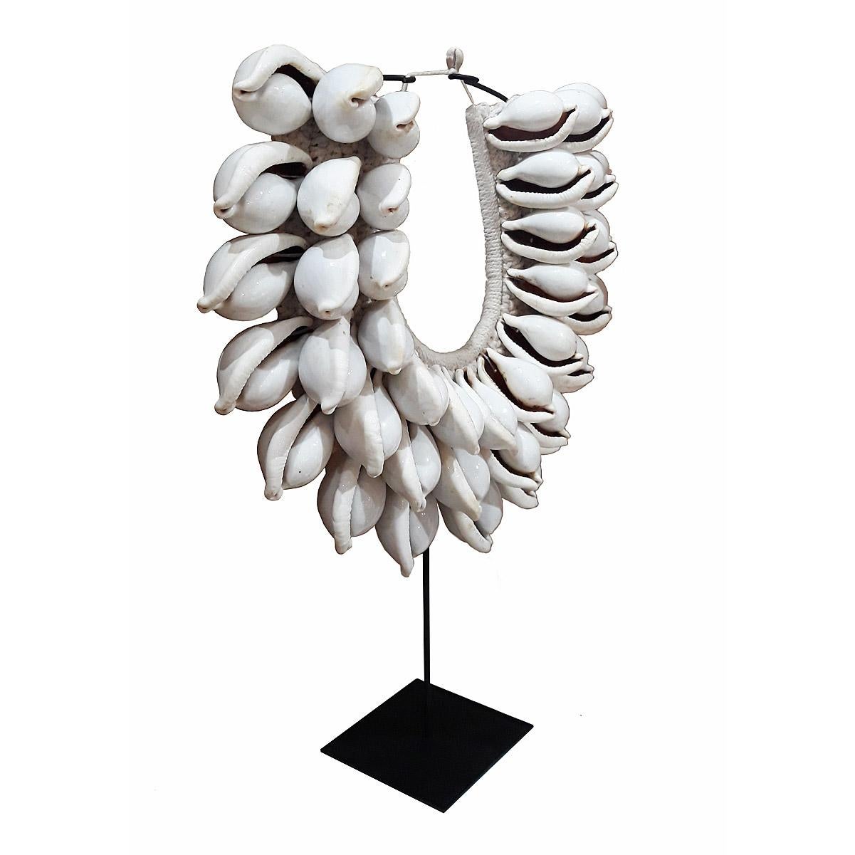A decorative seashell necklace from Bali, Indonesia, contemporary. 

The large, white Egg Cowry shells are delicately attached to a handwoven cotton / raffia circular base. Mounted in a black metal stand. 

This species of sea snail which