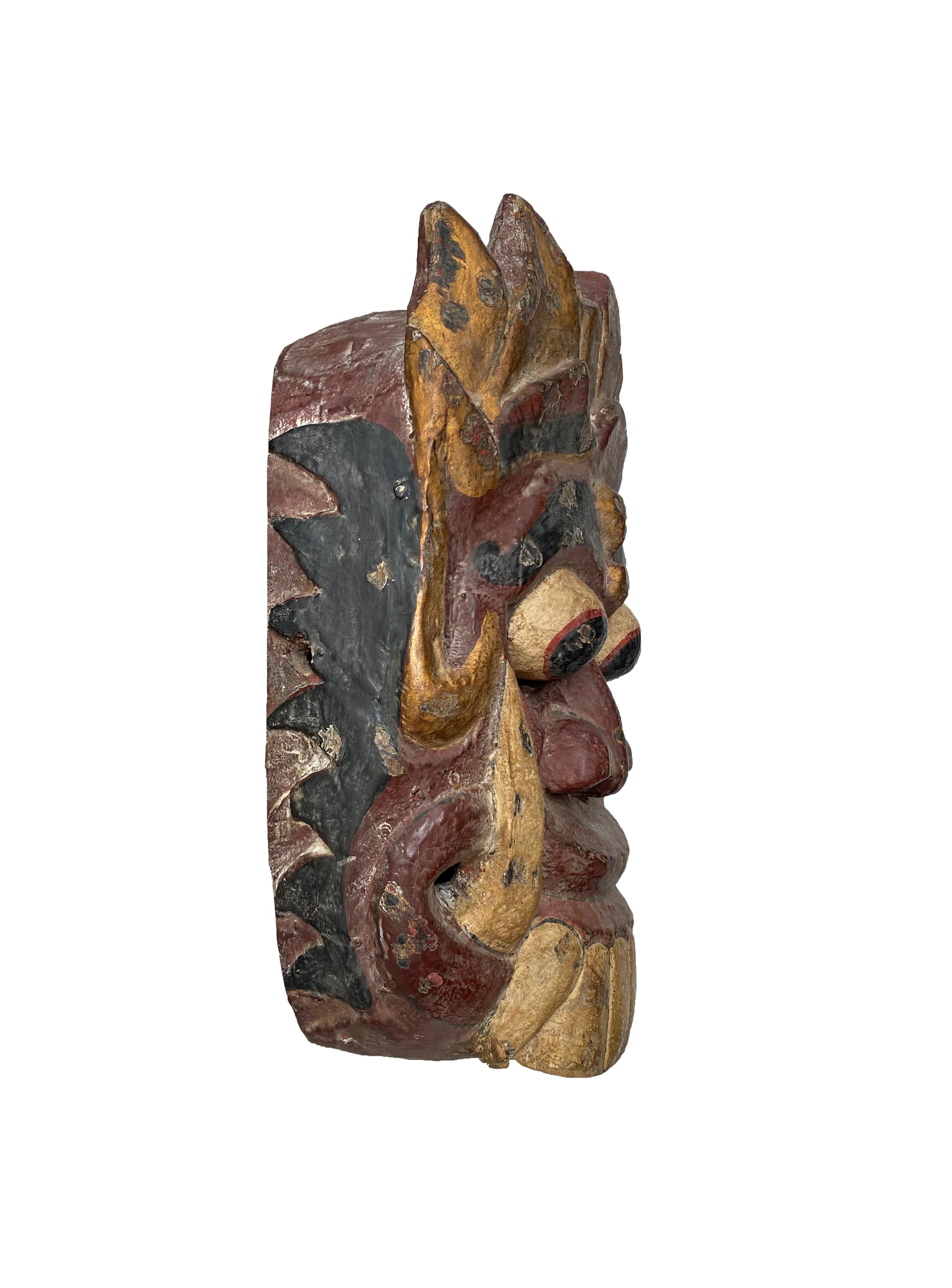 Diese handgeschnitzte Maske stammt von der Insel Bali und stellt Rangda dar, die Dämonenkönigin der balinesischen Hindu-Mythologie. Diese Maske wurde bei Zeremonien und/oder Tanzaufführungen verwendet. Sie zeigt eine Mischung aus Burgunder, Gold und