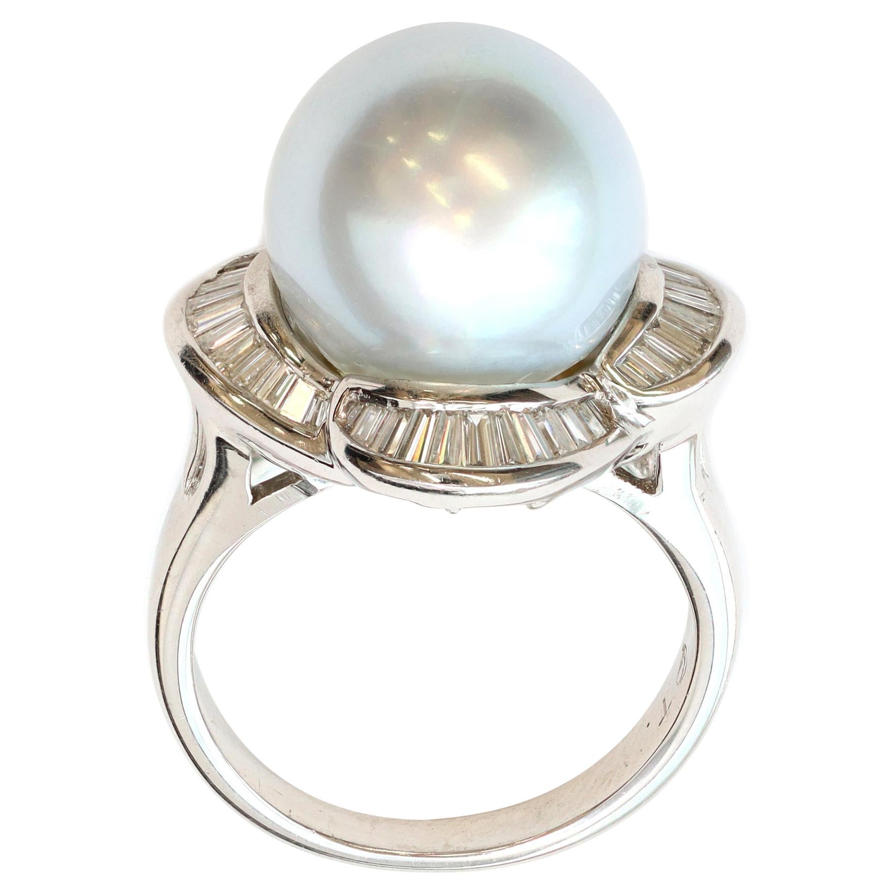 A ballerina style cocktail ring circa 1980 featuring a round south sea pearl with baguette diamonds set in platinum in a scalloped style mounting. The large white silvery pearl presents minor surface inclusions and measures 13 millimeters. The