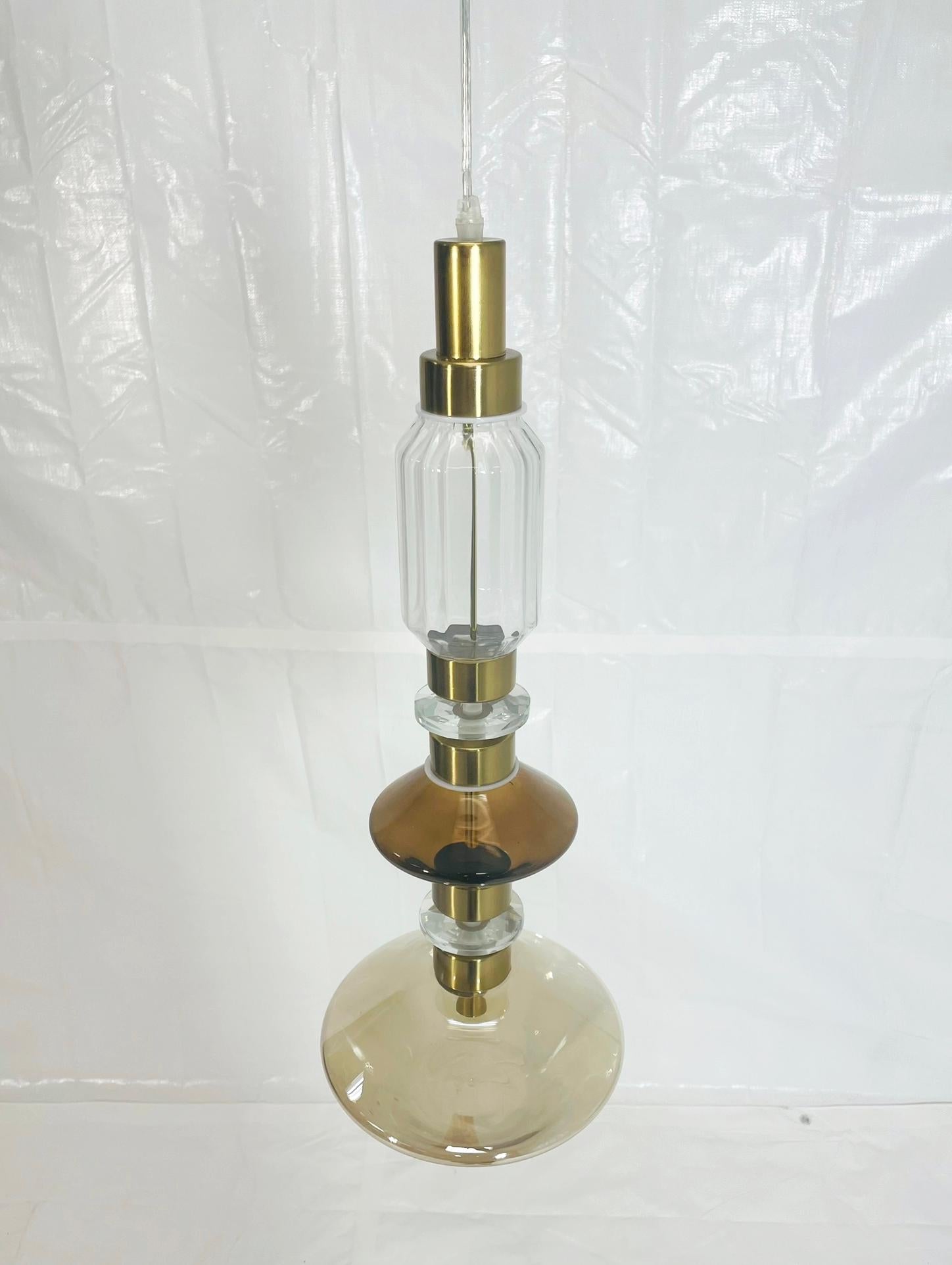 Elegant and sculptural pendant light from the Ballet collection, designed by Massimiliano Raggi for Sicis and handcrafted in Italy. The pendant features a refined composition of clear, amber, and smoky blown glass forms, joined by brushed brass