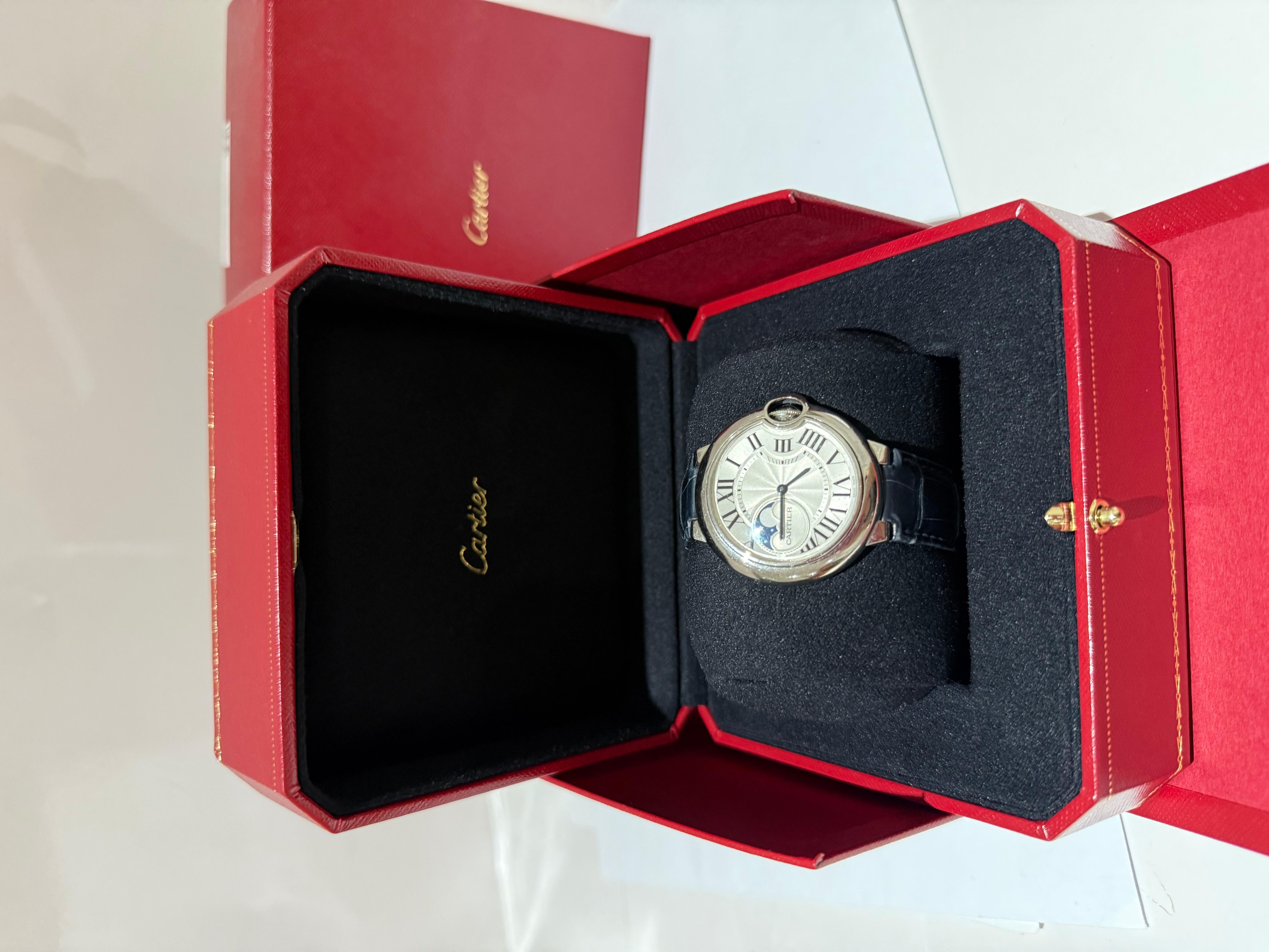 Ballon Bleu de Cartier watch, 37 mm. Mechanical movement with automatic winding, moon phases. Case in steel, fluted crown set with a synthetic cabochon-shaped spinel. Silvered guilloché dial. Moon phases at 9 o’clock. Blued-steel sword-shaped hands.