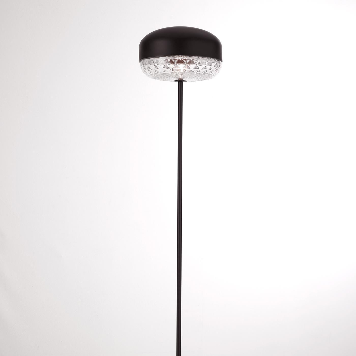 Showcasing a minimal and harmonious metal structure with a matte black finish, the Balloton floor lamp conveys a decidedly modern glamour with an accent of antique tradition. A black, slender stem rises from a circular base that visually